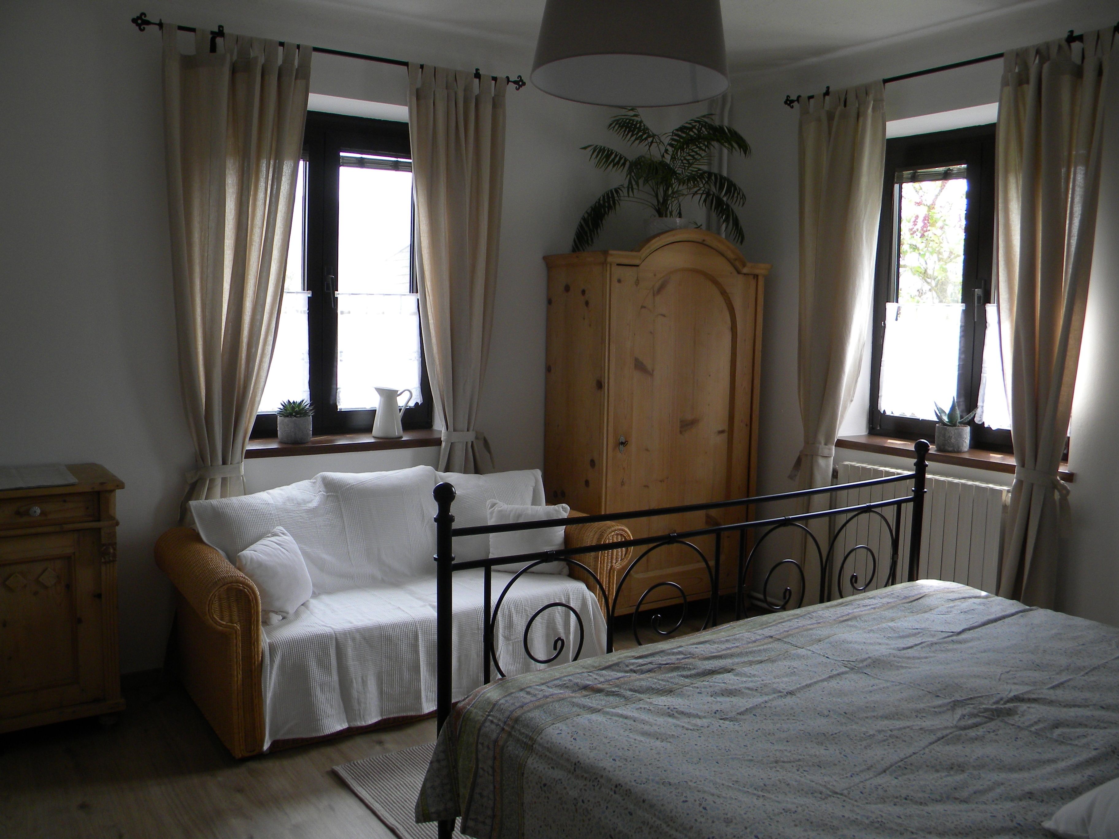 Ein gemütliches Schlafzimmer mit einem Metallbett, einem Sofa, einem Holzschrank und zwei Fenstern mit Vorhängen.