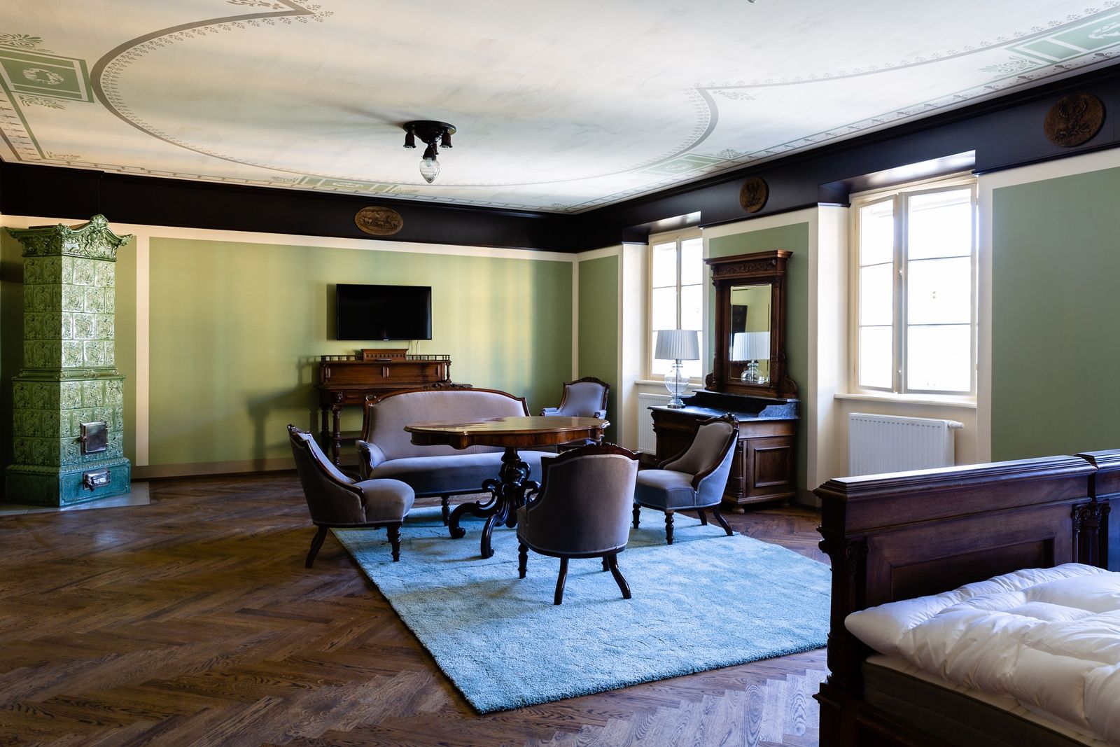 Elegantes Zimmer mit antiken Möbeln, grünem Kachelofen und Teppich.