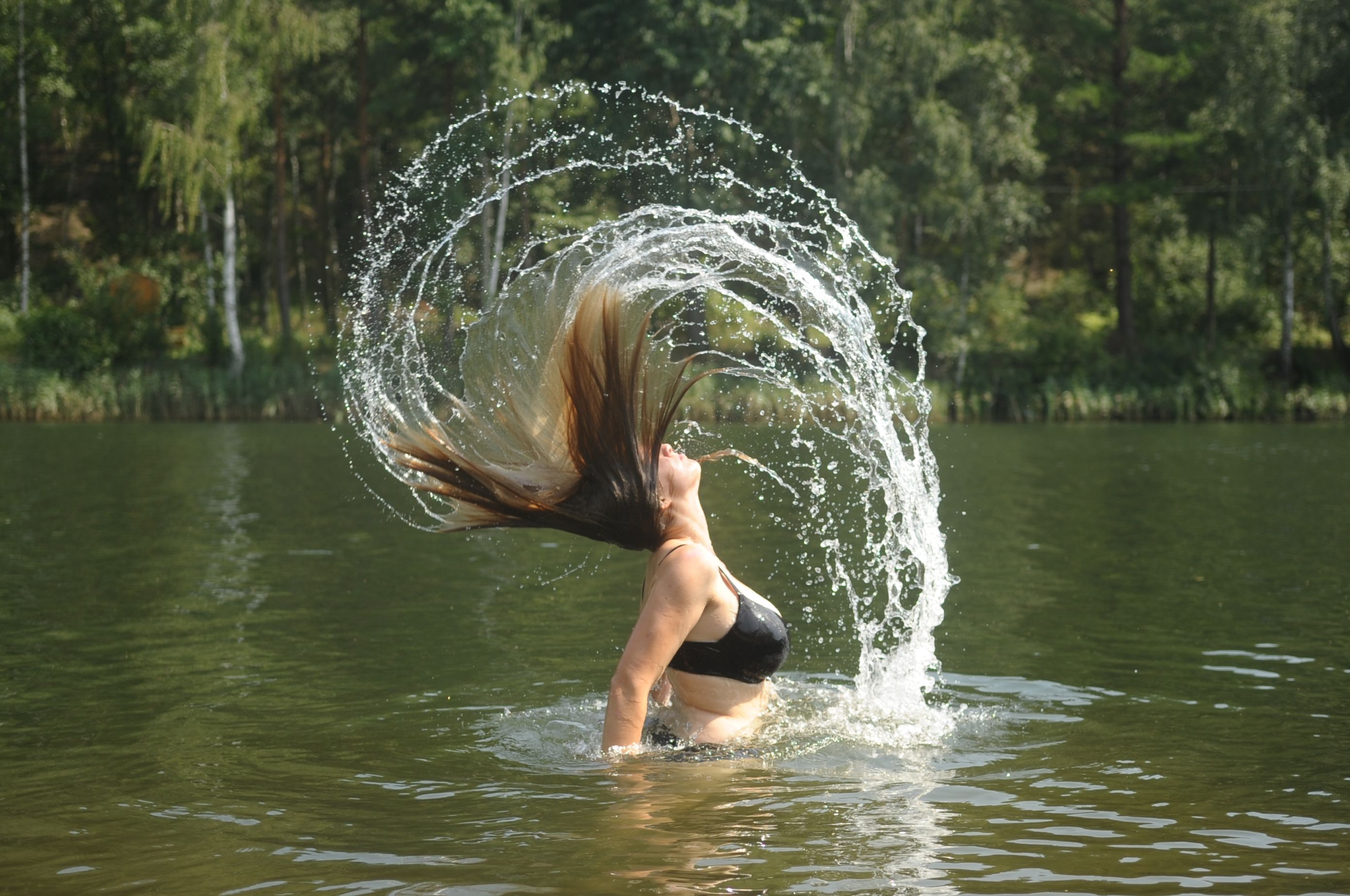 Frau wirft ihre Haare im Wasser zurück, wodurch ein Wasserspritzer entsteht.