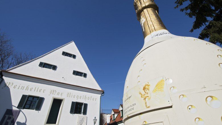 Weinkeller Max Riegelhofer und große Sektflasche im Freien.