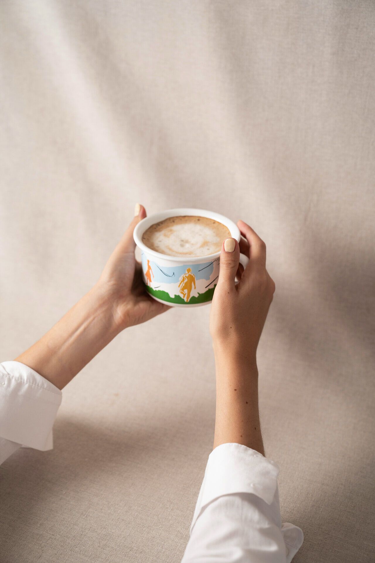 Hände halten Tasse mit limitiertem, buntem Niederösterreich-Design von Ries Keramik in den Händen. 