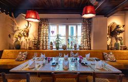 Gemütlicher Essbereich mit großen Fenstern, grünen Polstermöbeln und Pflanzen, mit Blick auf die Landschaft.