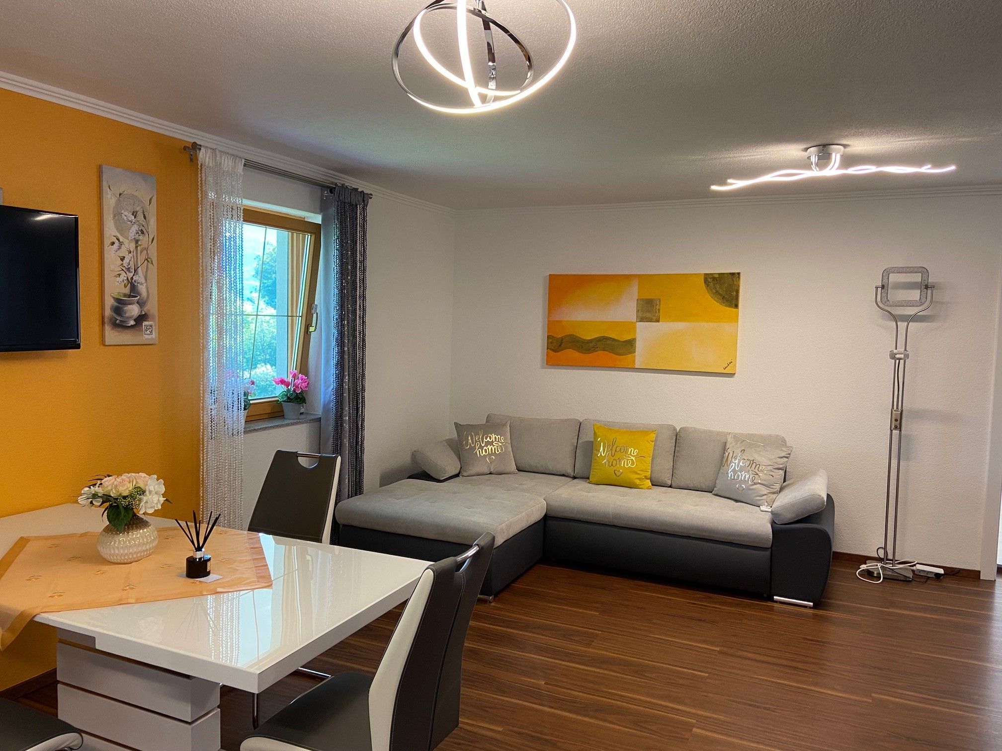 Wohnküche mit grauer ausziehbarer Couch, Esstisch und Dekorationen.