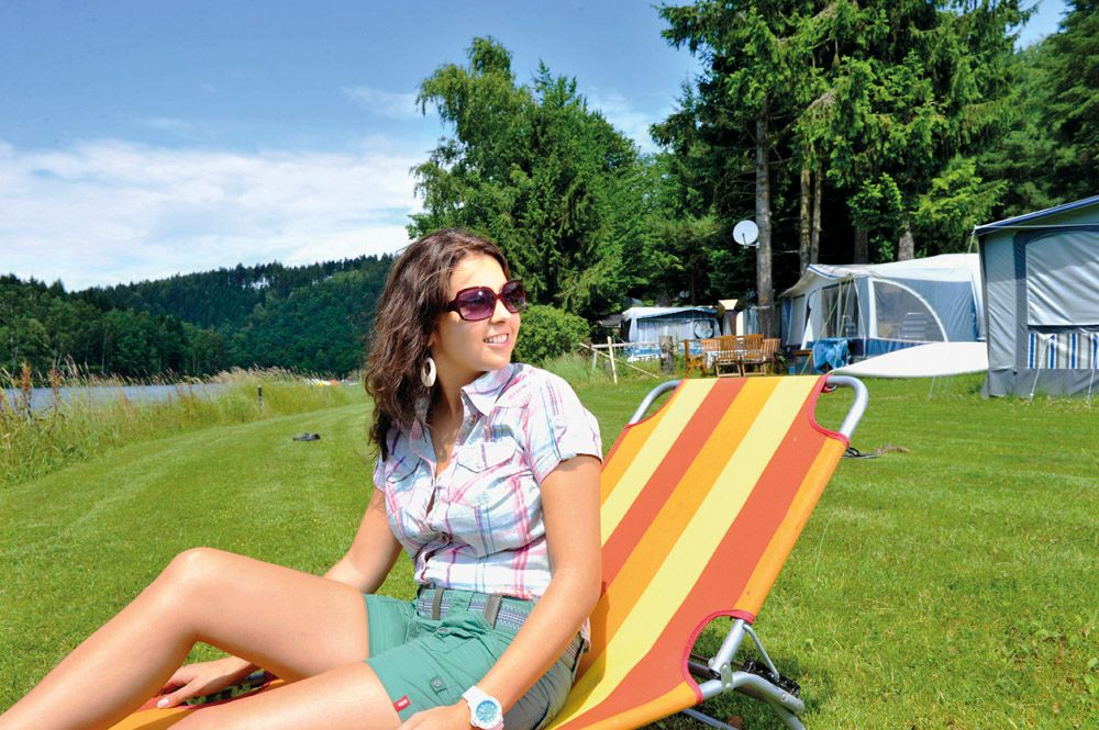 Frau entspannt auf Liegestuhl beim Campingplatz am See.
