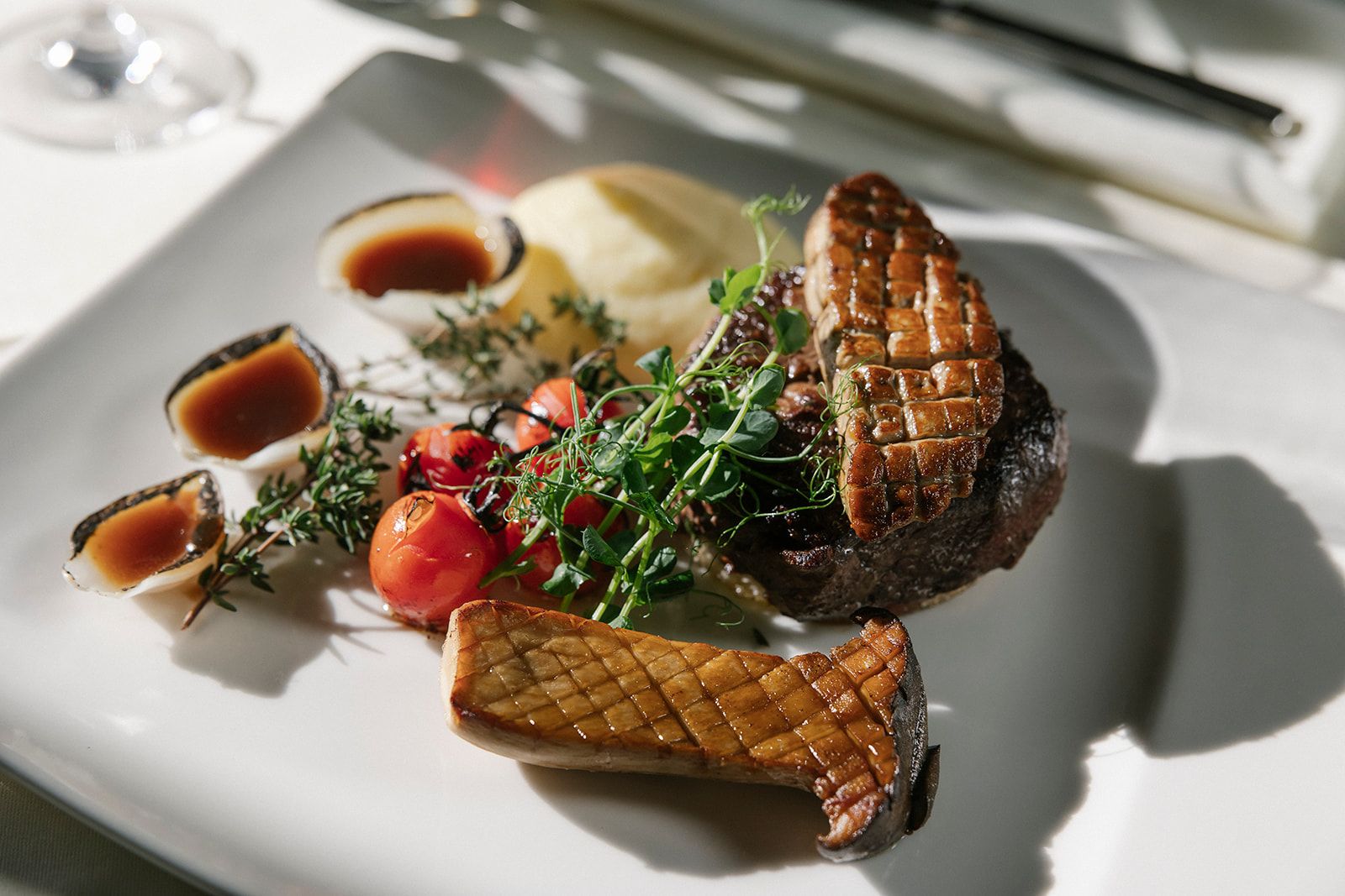 Gourmetgericht mit Steak, Pilz, Tomaten und Soße auf einem weißen Teller.