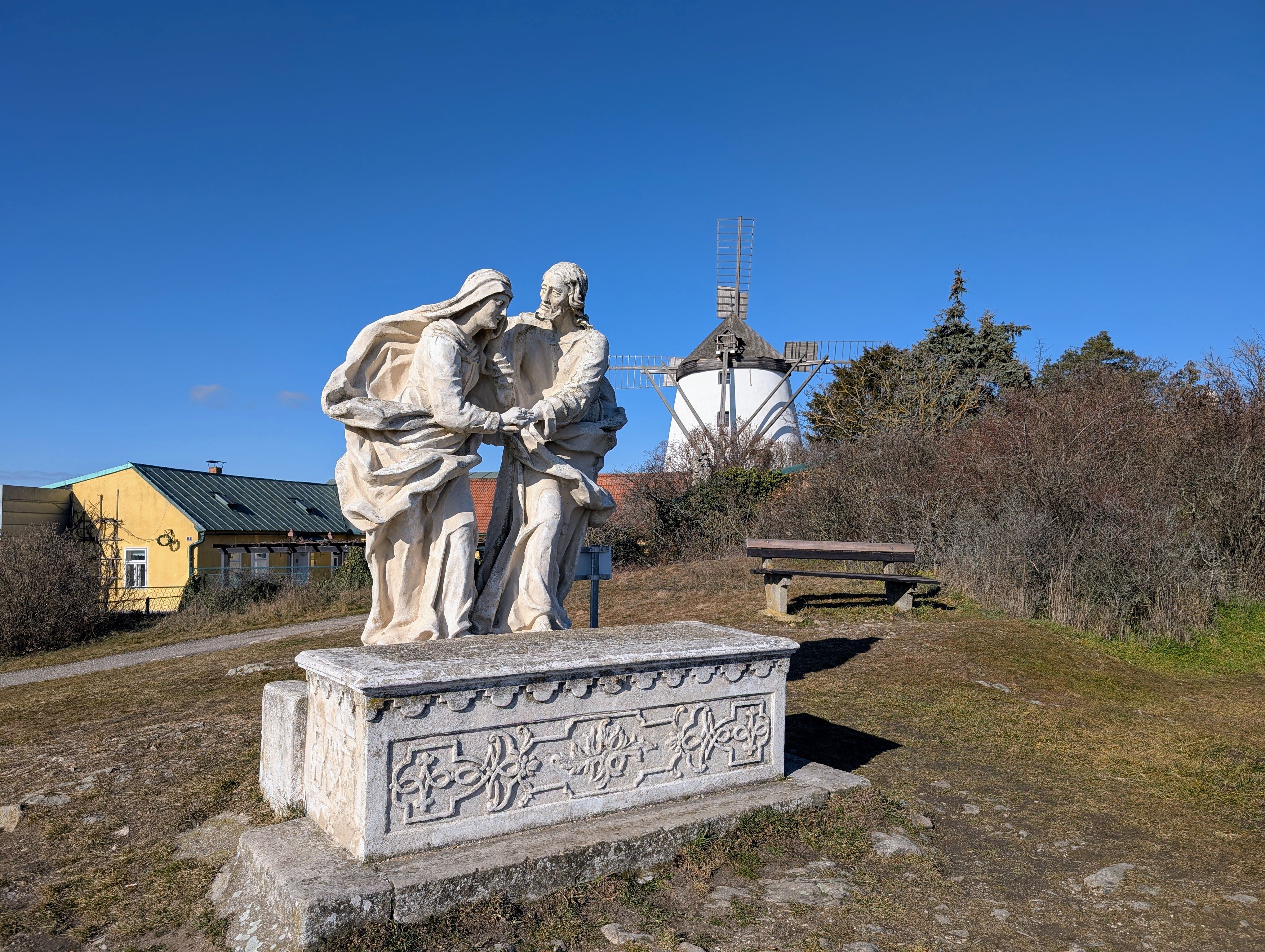 Steinskulptur auf einem Hügel mit einer Windmühle im Hintergrund.