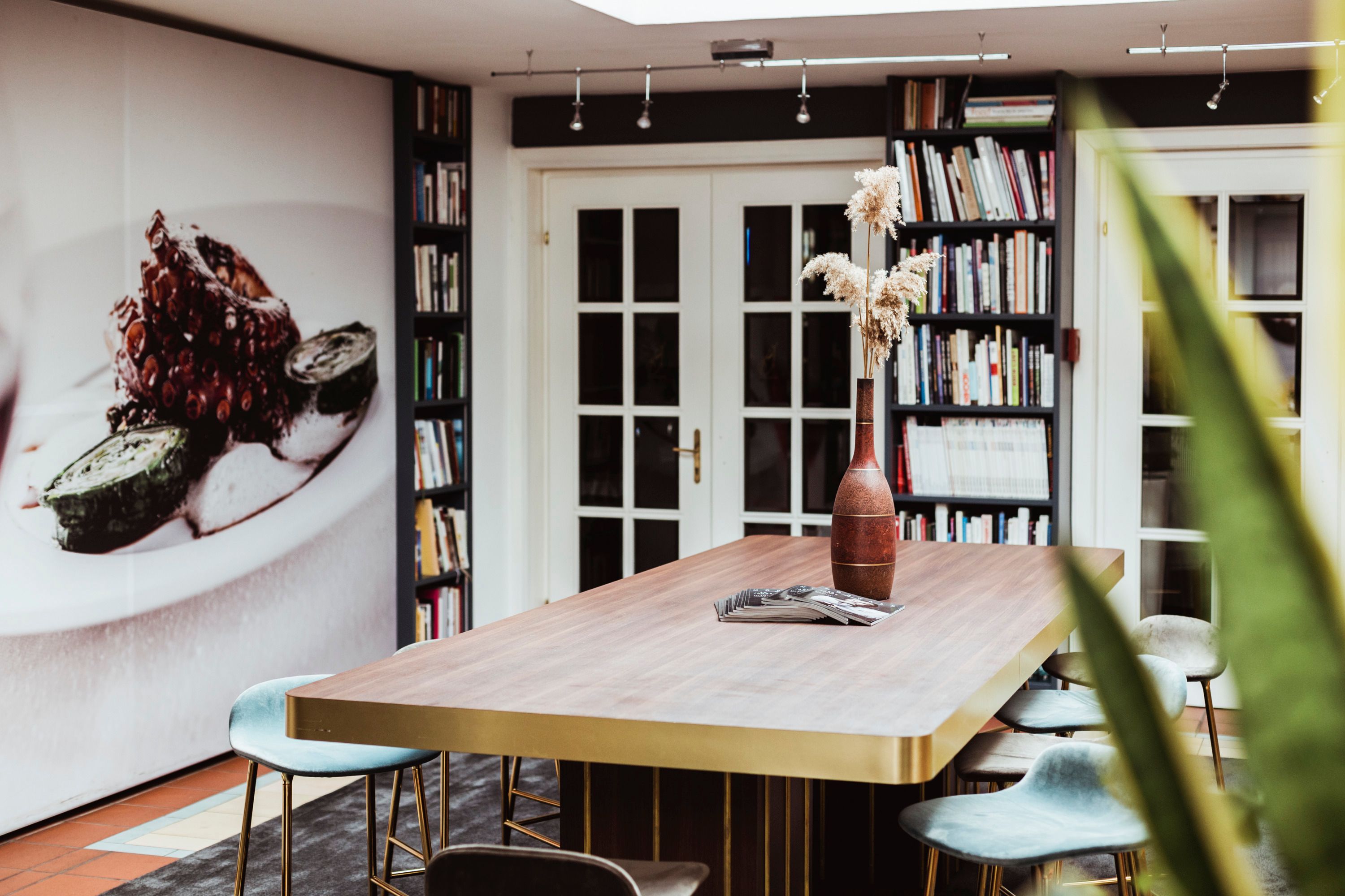 Moderner Raum mit großem Tisch, Bücherregalen und Wandbild.