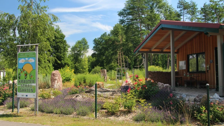 Eingang zum Kräuterschaugarten mit Schild und kleinem Gebäude.