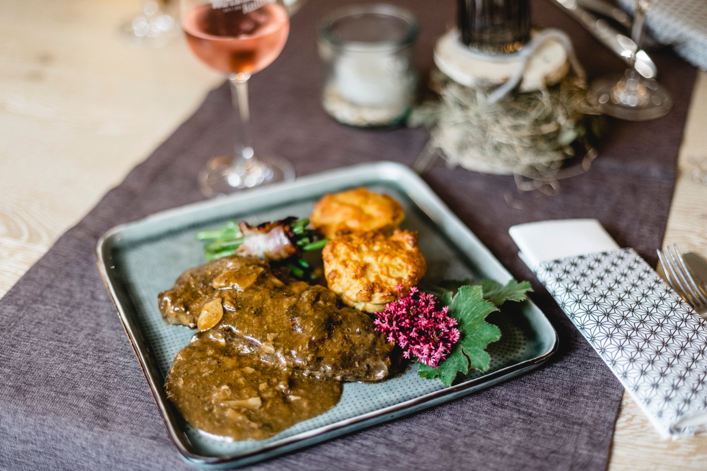 Ein Teller mit Rostbraten, gefüllt mit Steinpilzen, serviert mit Beilagen und einer Blume als Dekoration.