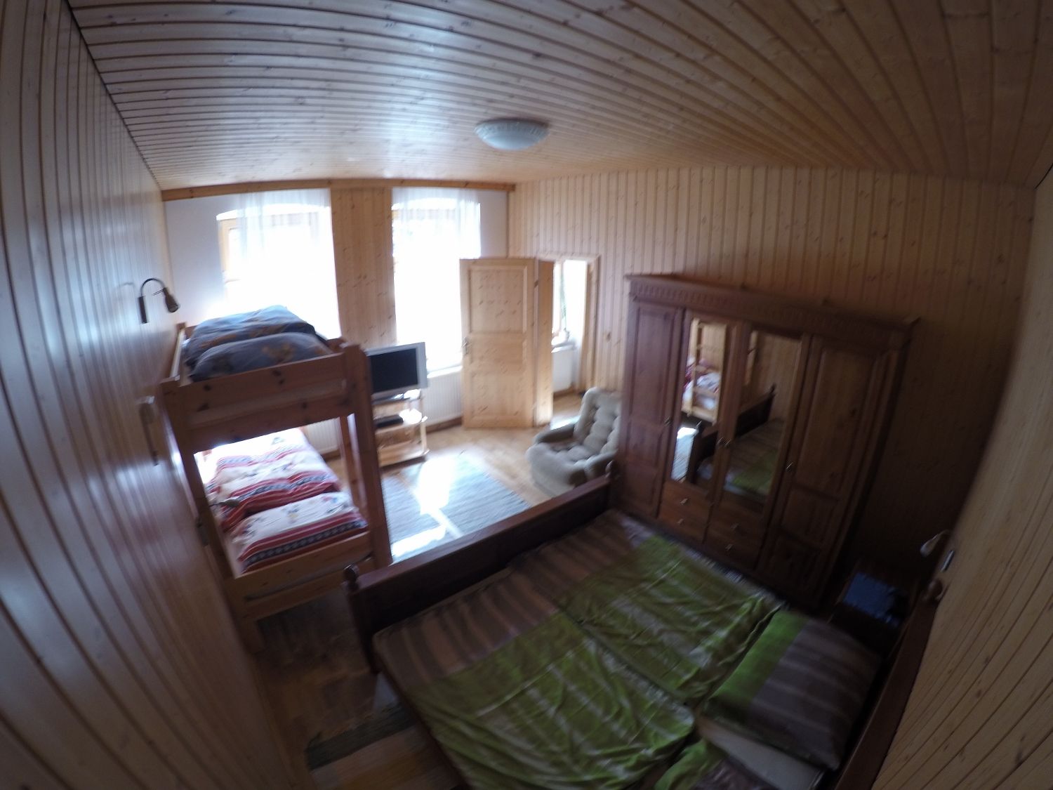 Holzvertäfeltes Schlafzimmer mit Etagenbett, Doppelbett, Kleiderschrank und Fernseher.