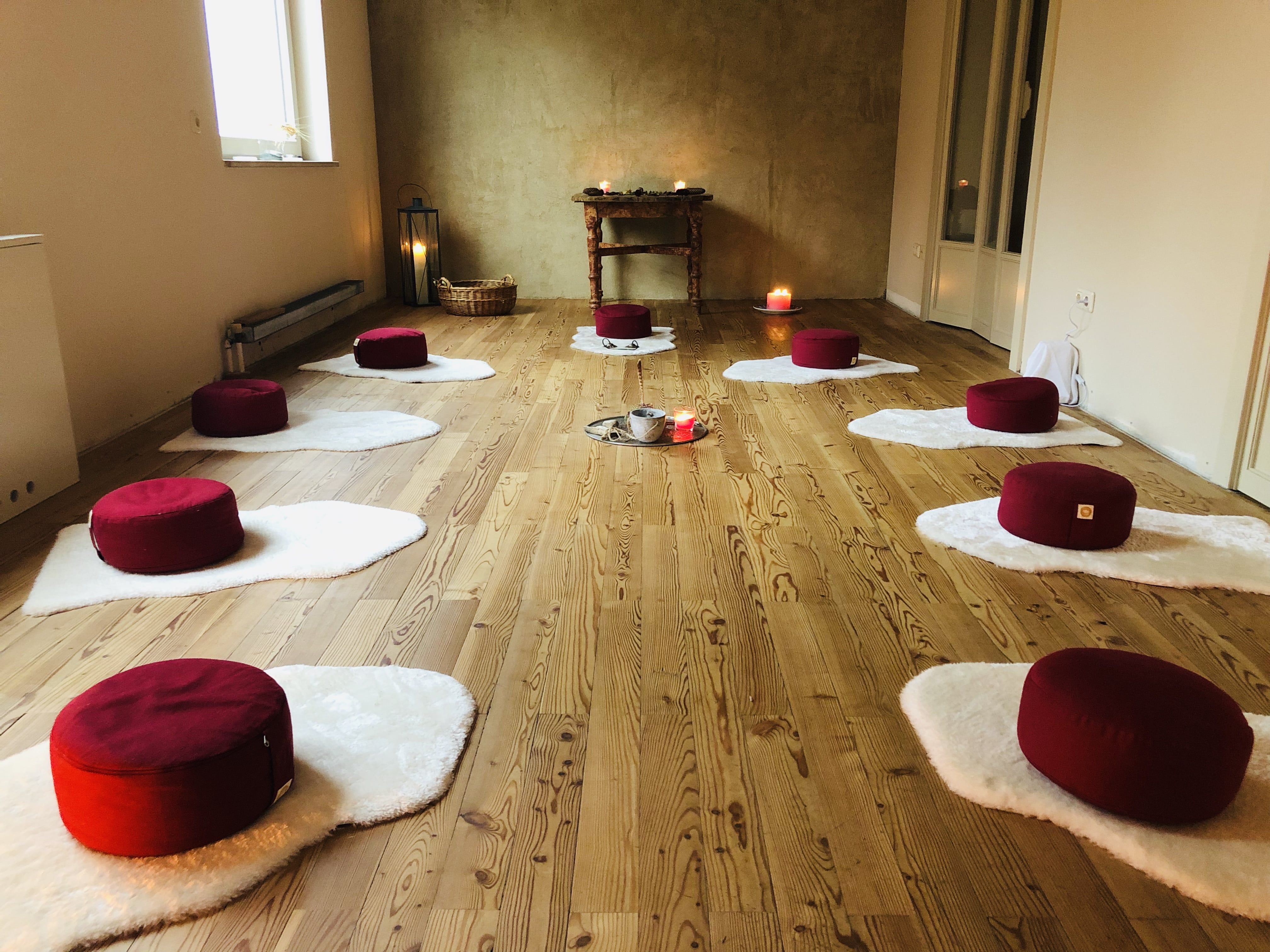 Meditationsraum mit roten Kissen auf weißen Matten, Kerzen und Holzfußboden.