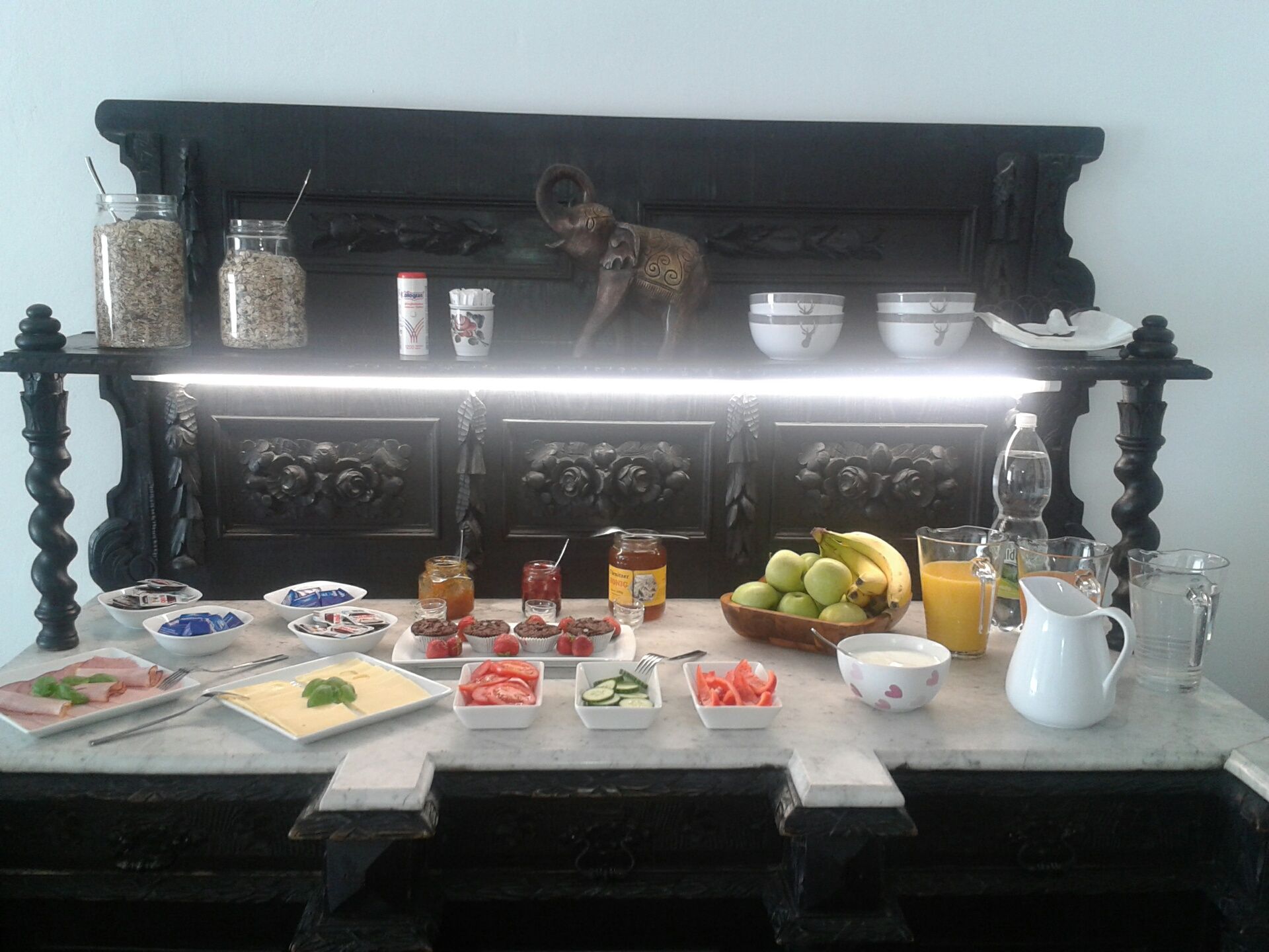 Frühstücksbuffet mit Obst, Aufschnitt, Käse, Marmelade und Getränken auf einem dekorativen Tisch.