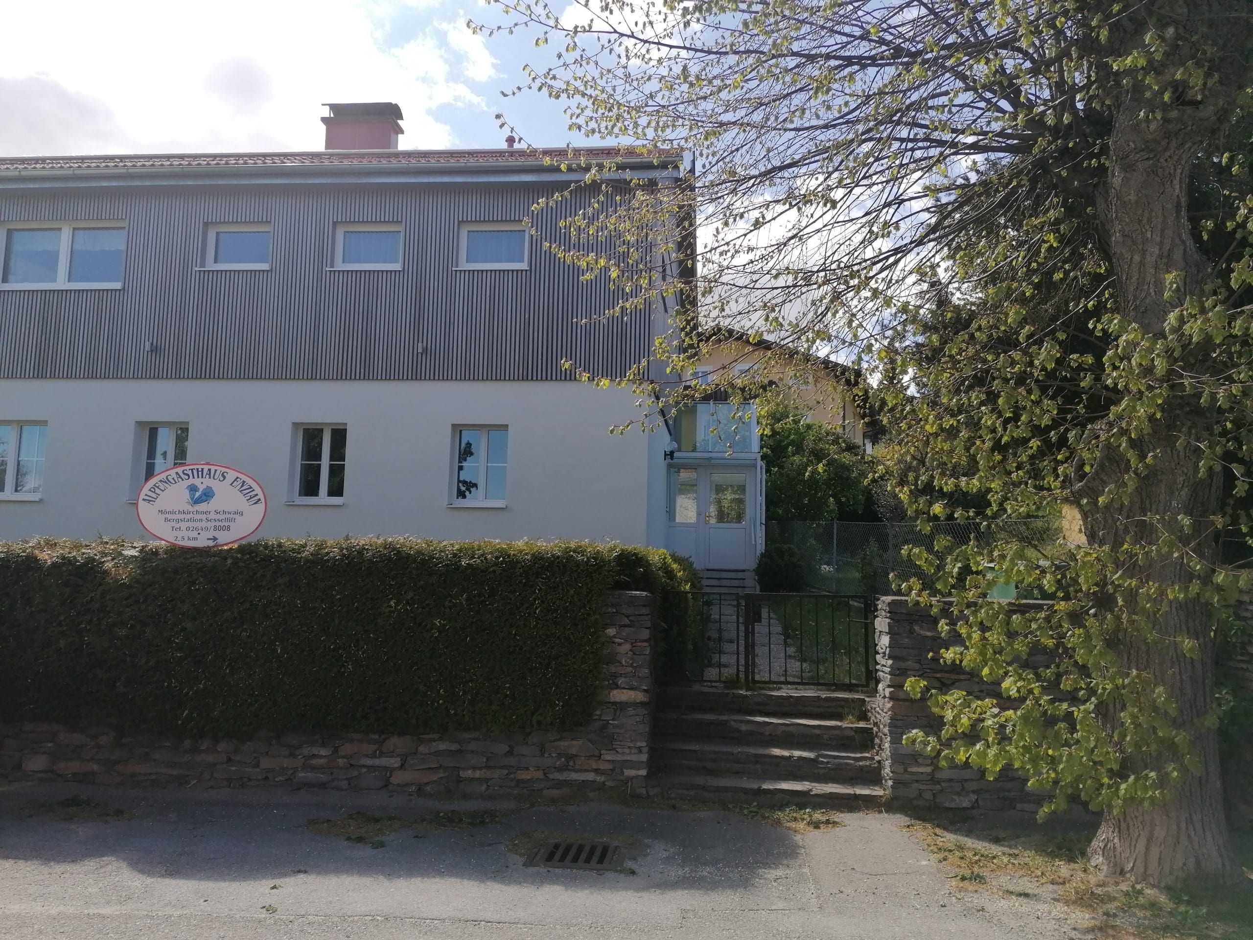 Zweistöckiges Gebäude mit Schild 'Alpengasthaus Ewin' und Garten.