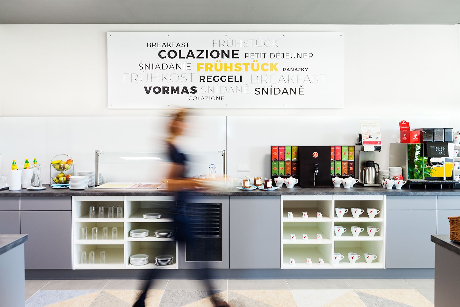 Eine lange graue Theke mit Tassen und Geschirr. Auf der Theke befindet sich Alles für Kaffee und Tee.