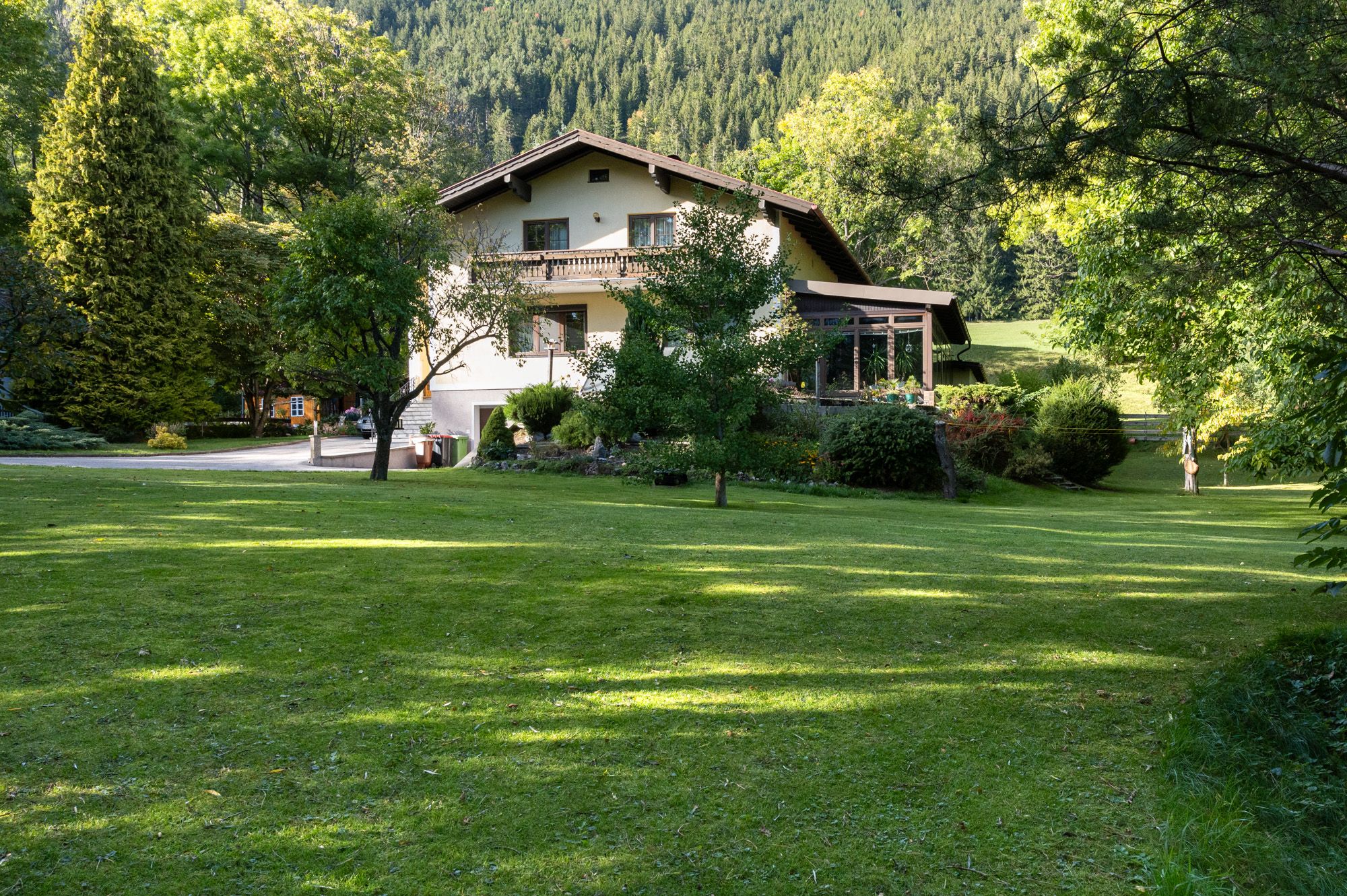 Ein zweistöckiges Ferienhaus inmitten eines grünen Gartens mit Bäumen und Wiese, umgeben von Wald.