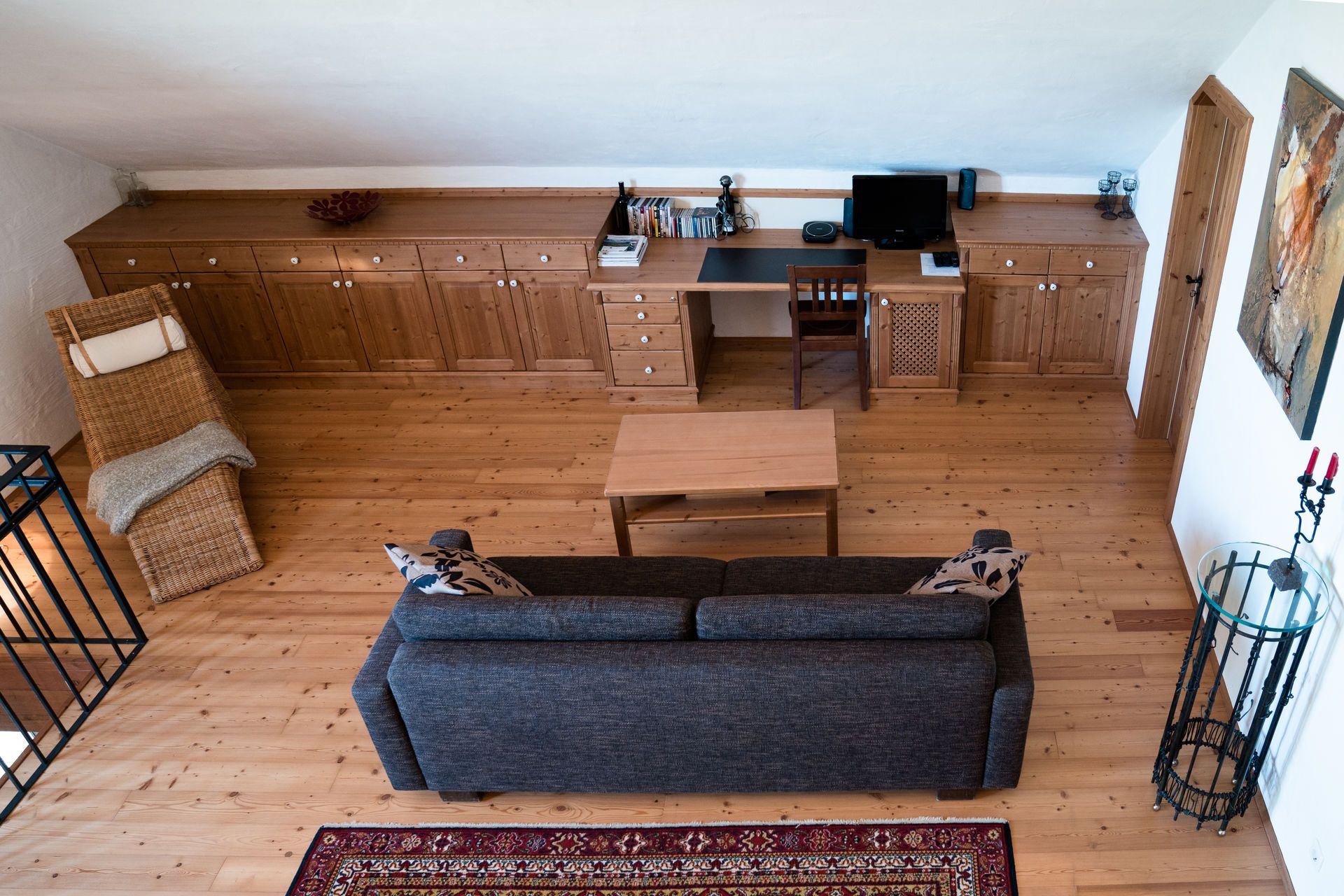 Wohnzimmer im Obergeschoss mit Holzboden, Sofa, Tisch, Schreibtisch und Stuhl.