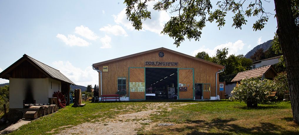 Außenansicht des Dorfmuseums Maiersdorf mit Holzhäusern und Bäumen.