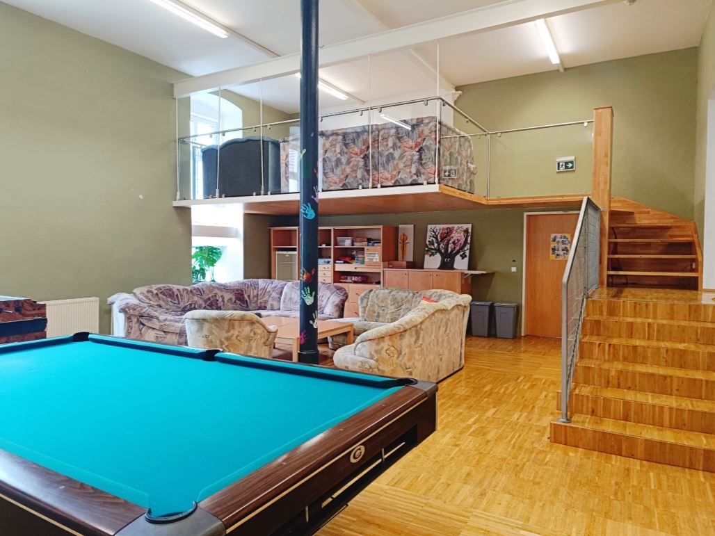 Ein Jugendraum mit Billardtisch, Sofas und einer Empore mit Treppe.