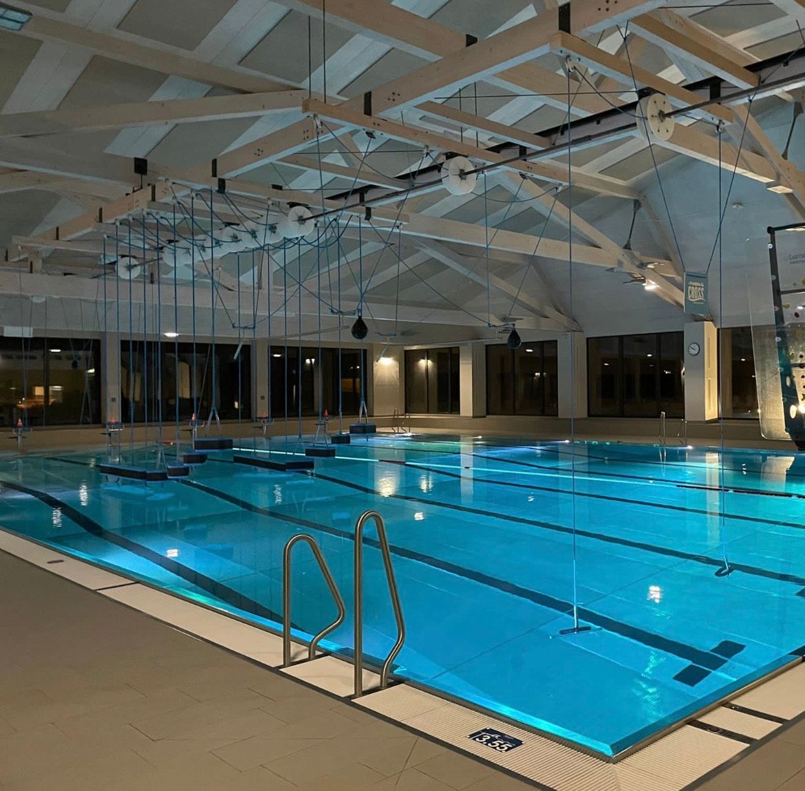 Ein beleuchtetes Hallenbad mit einem leeren Schwimmbecken und einer Kletterwand im Hintergrund.