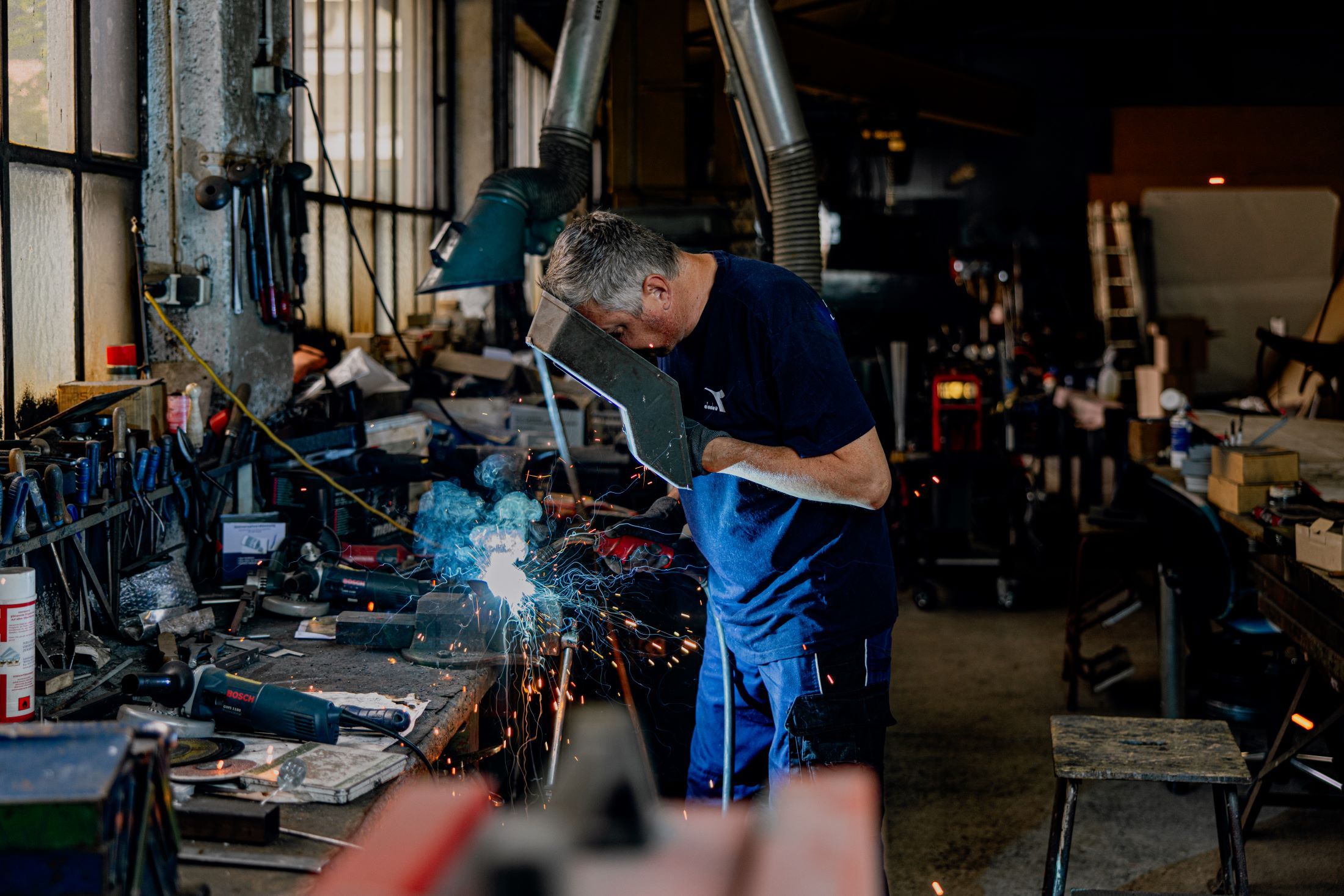 Ein Mann schweißt in einer Werkstatt, umgeben von Werkzeugen und Funken.