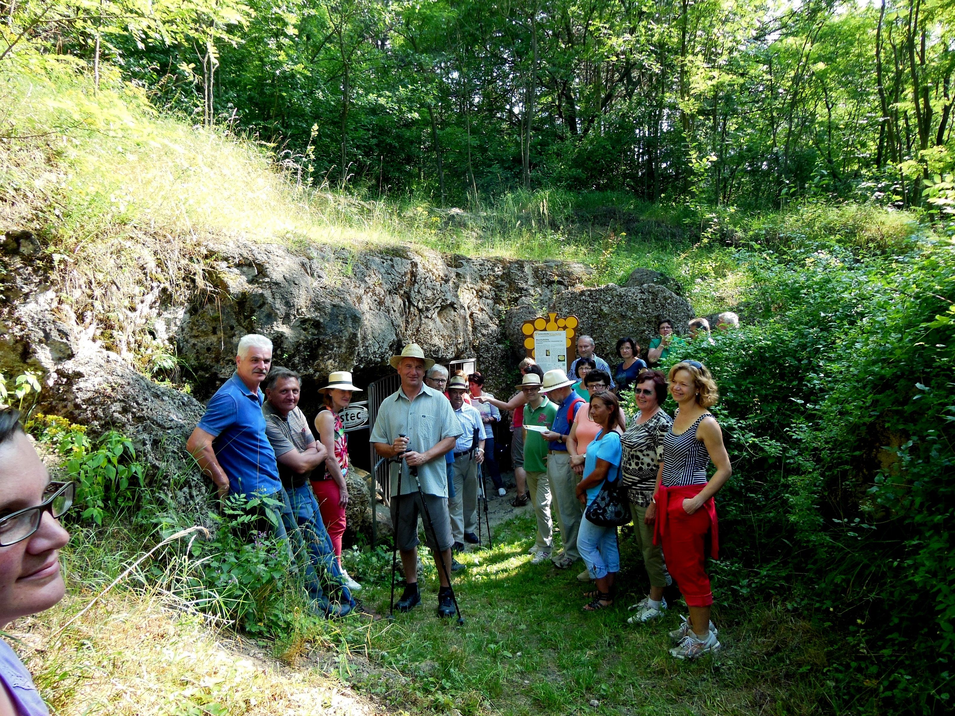 Gruppe von Menschen vor einer Höhle im Grünen.