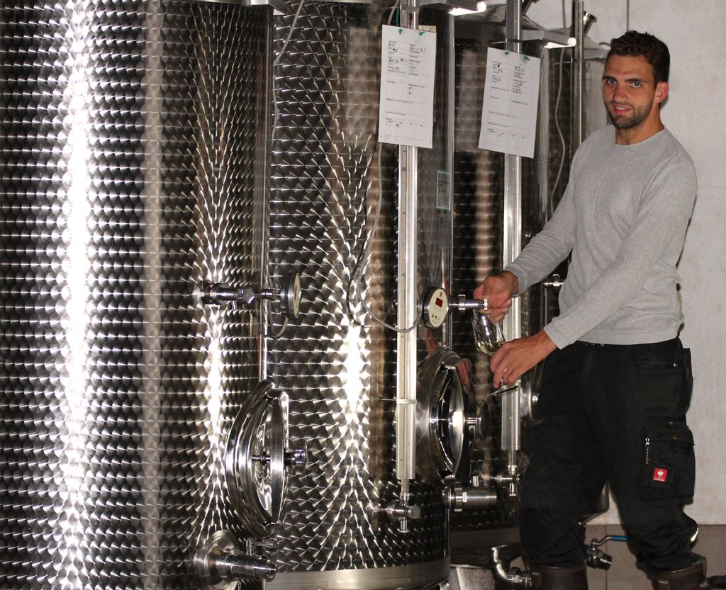 Ein Mann zapft Wein aus einem Edelstahltank in einem Weinkeller.
