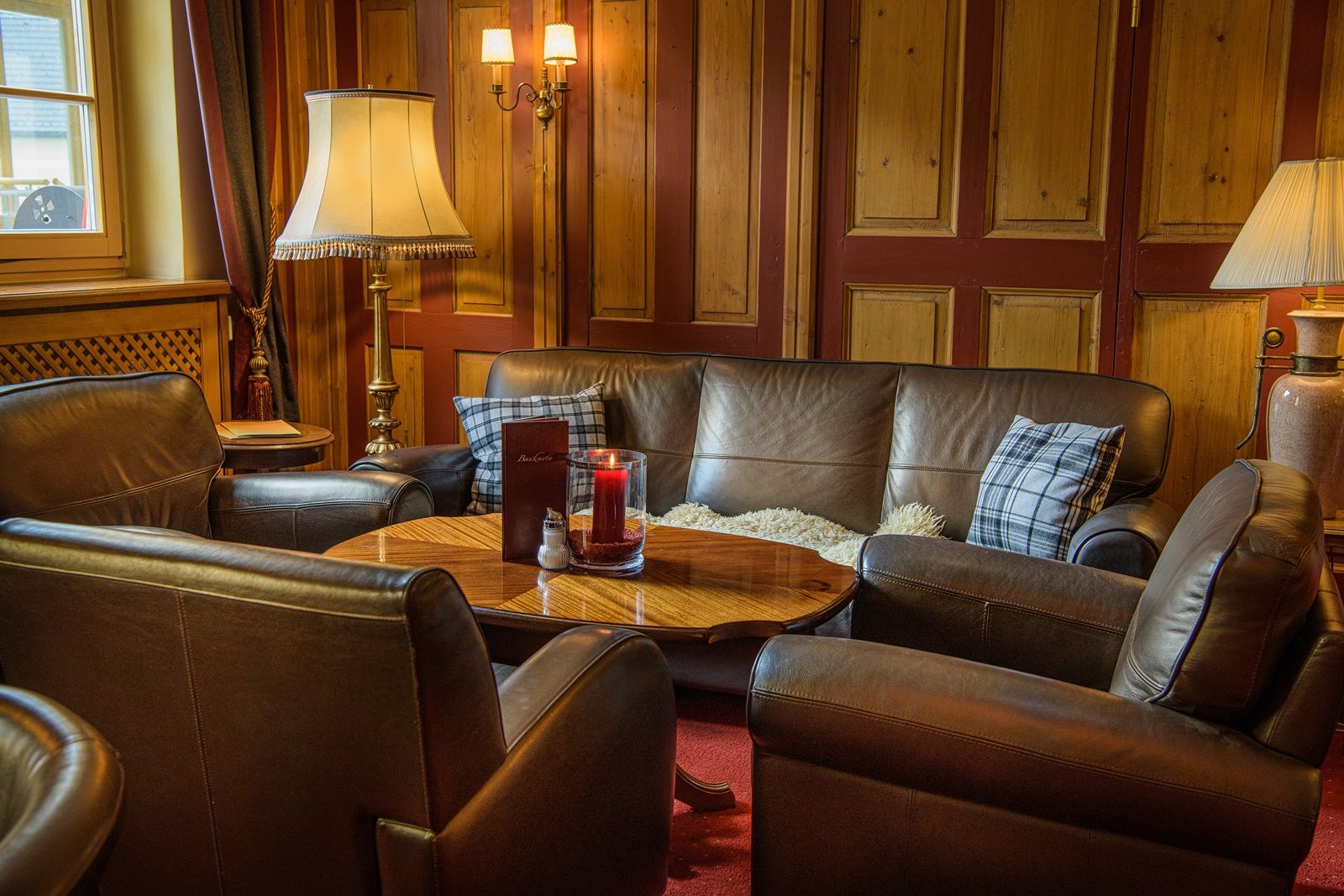 Gemütlicher Barbereich mit Ledersofas, Holztisch und Lampen.