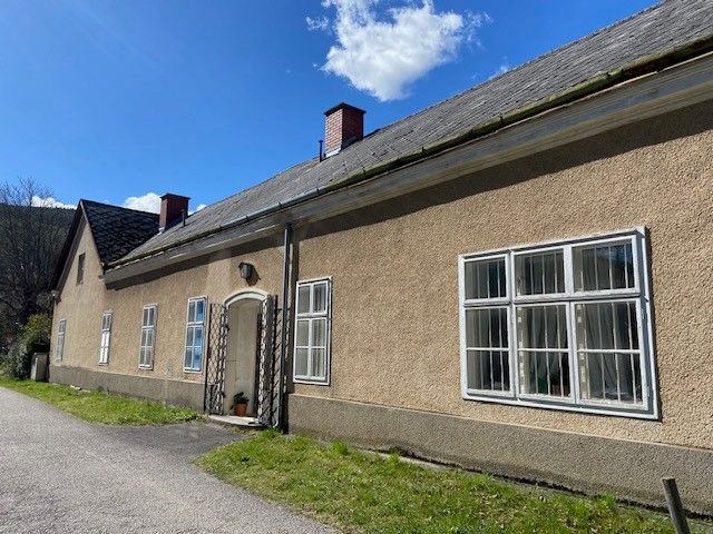 Langes, einstöckiges Gebäude mit mehreren Fenstern und einem Schrägdach unter blauem Himmel.