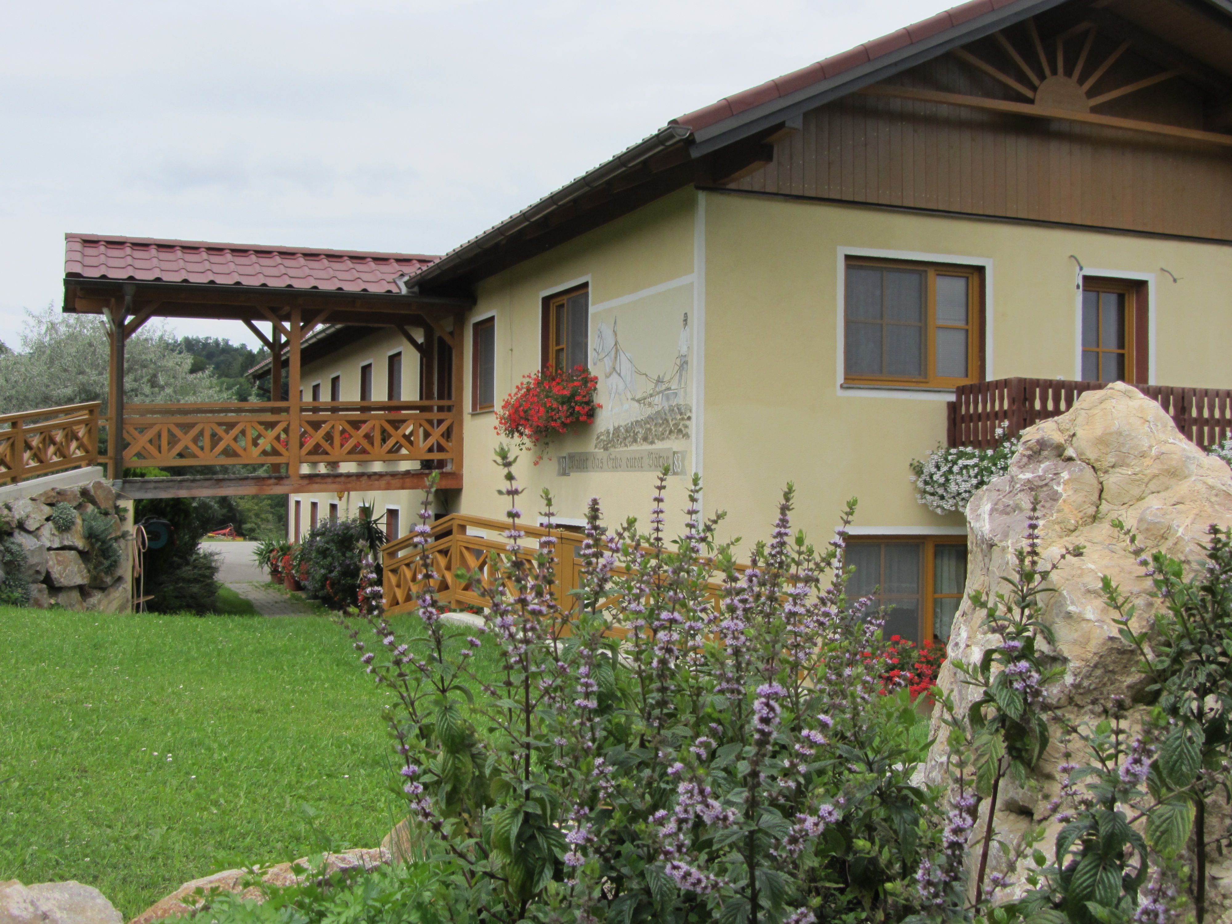 Ein gelbes Gebäude mit Holzbalkon und Blumen, umgeben von grüner Landschaft.