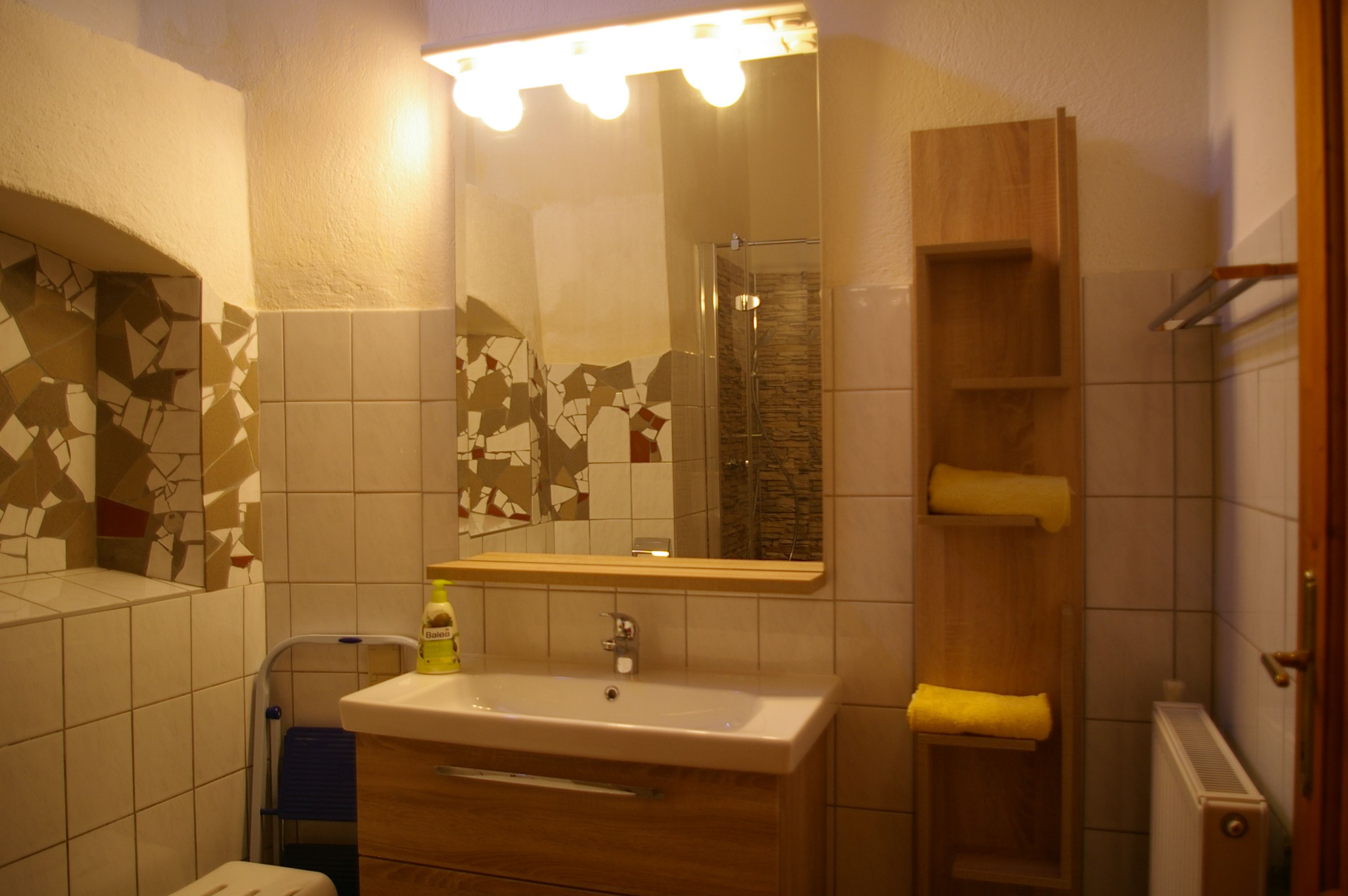 Badezimmer mit Spiegel, Waschbecken, Fliesen und Regal mit Handtüchern.
