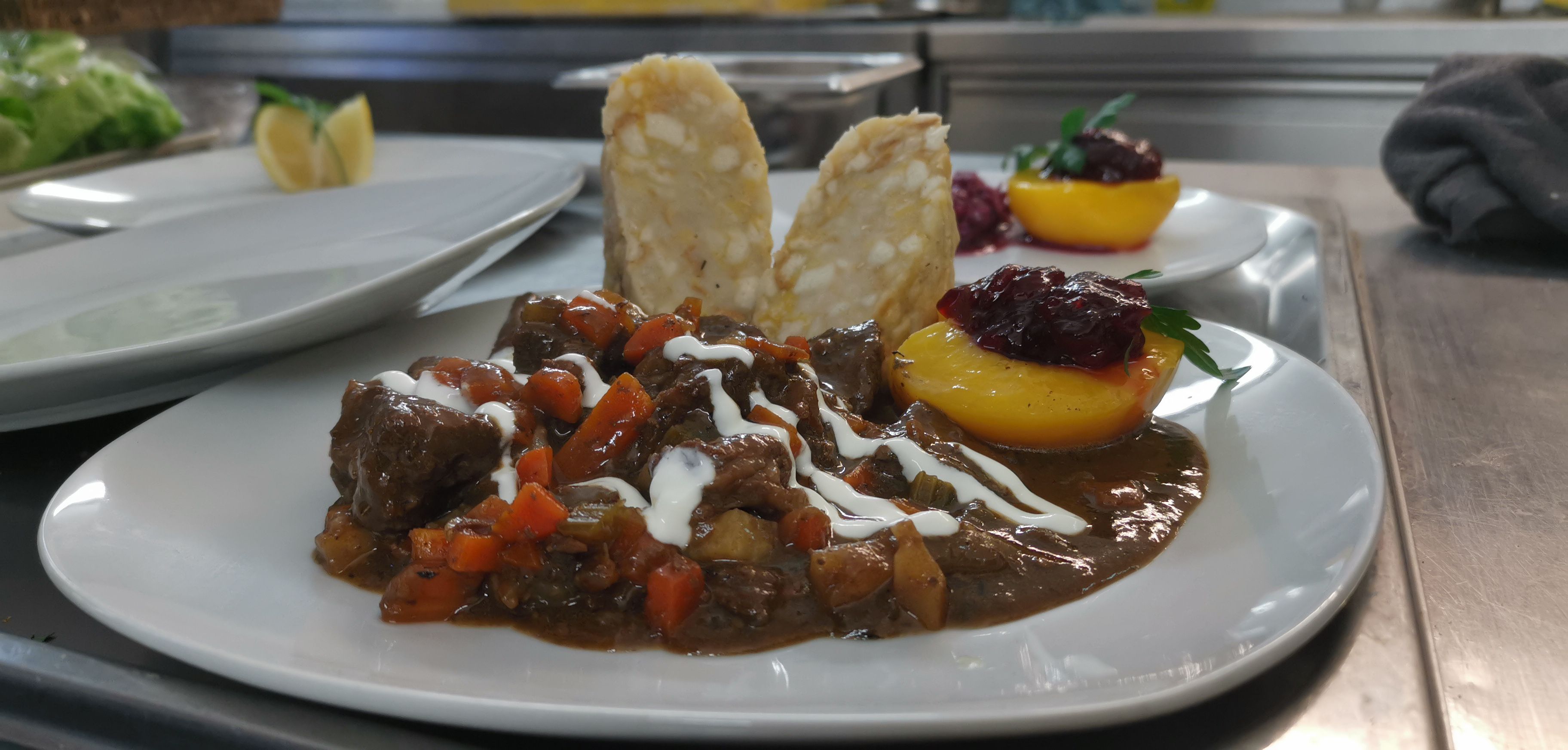 Ein Teller mit einem Fleischgericht, garniert mit Soße, Gemüse und einer Pfirsichhälfte mit Preiselbeeren.