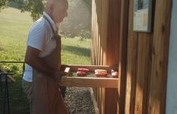 Ein leidenschaftlicher Koch bringt frische, handgemachte Köstlichkeiten aus der Region in die warme Abendsonne. Die sanften Hügel im Hintergrund versprechen ein unvergessliches kulinarisches Erlebnis, während der Duft von gegrilltem Fleisch die Luft erfüllt.