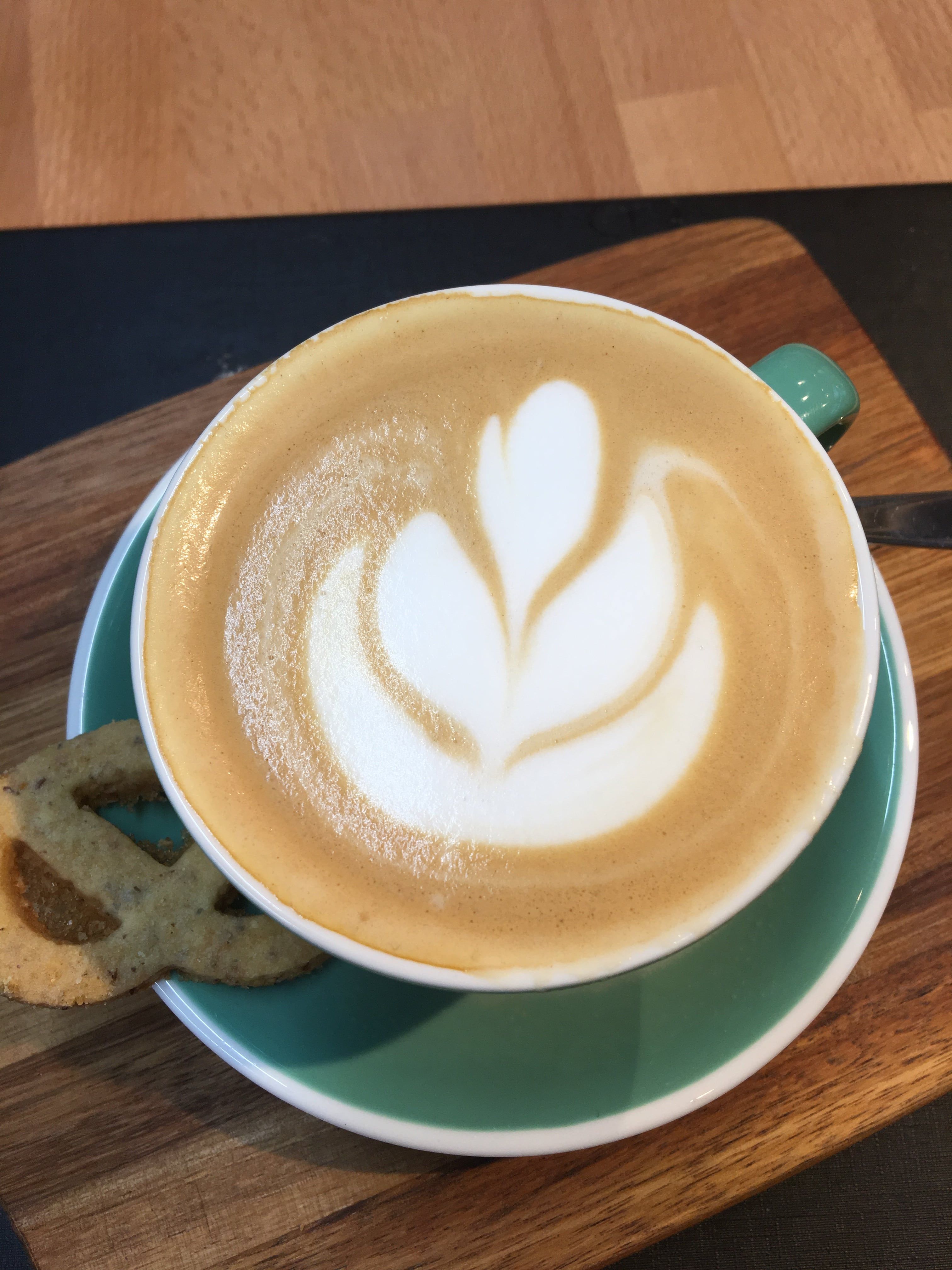 Cappuccino mit Latte Art in einer grünen Tasse auf einem Holzbrett.