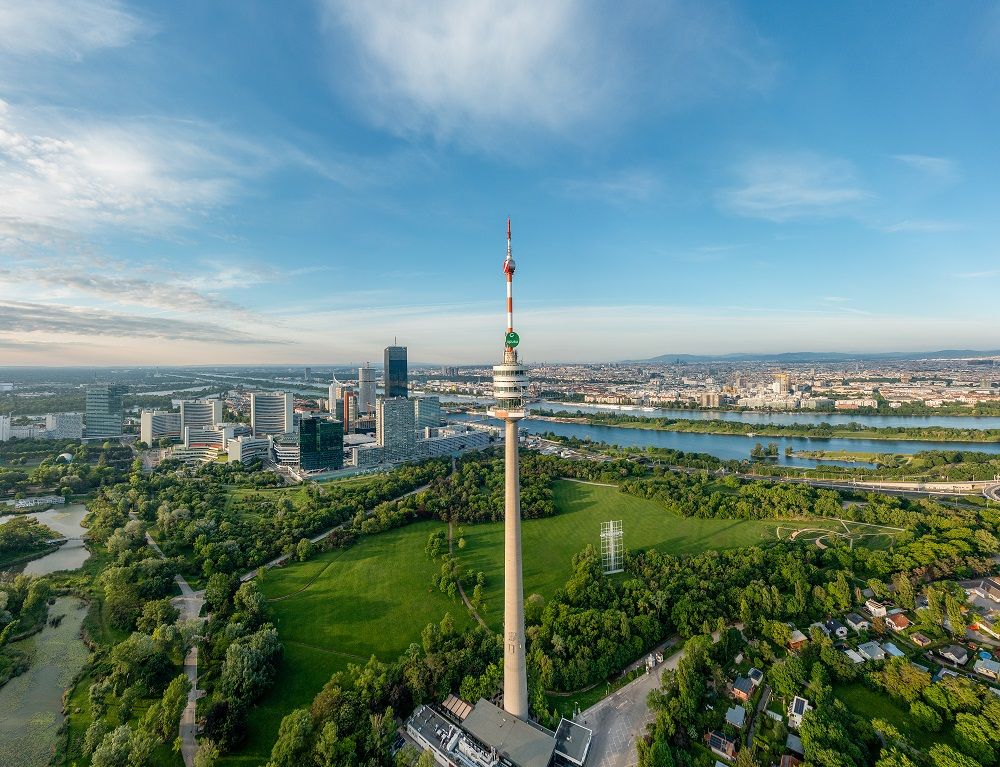 Luftaufnahme des Donauturms in Wien mit umliegender Stadtlandschaft und Donau.