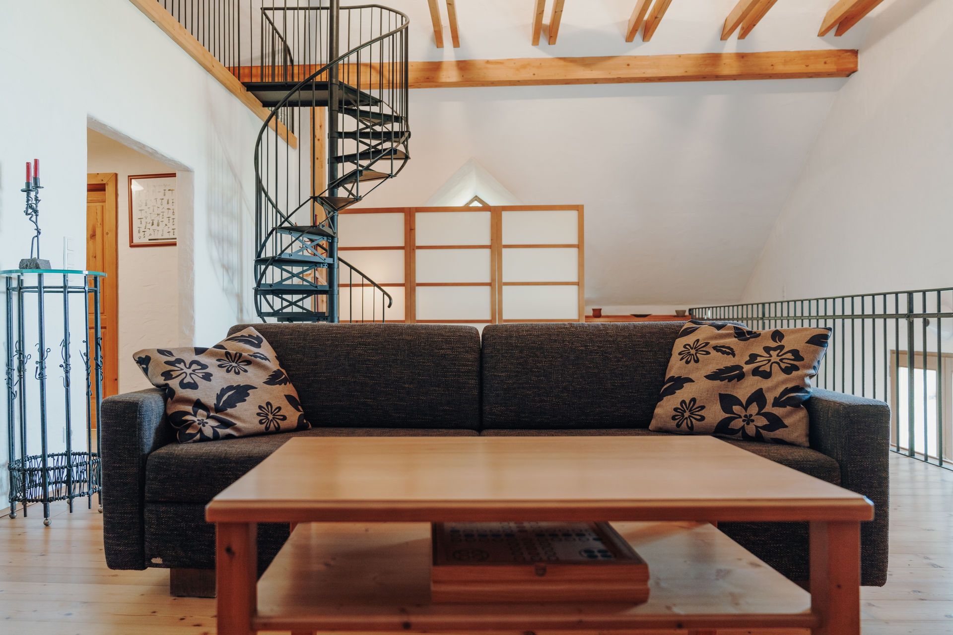 Wohnzimmer mit Schlafsofa, Holztisch und Wendeltreppe in einem Loft.