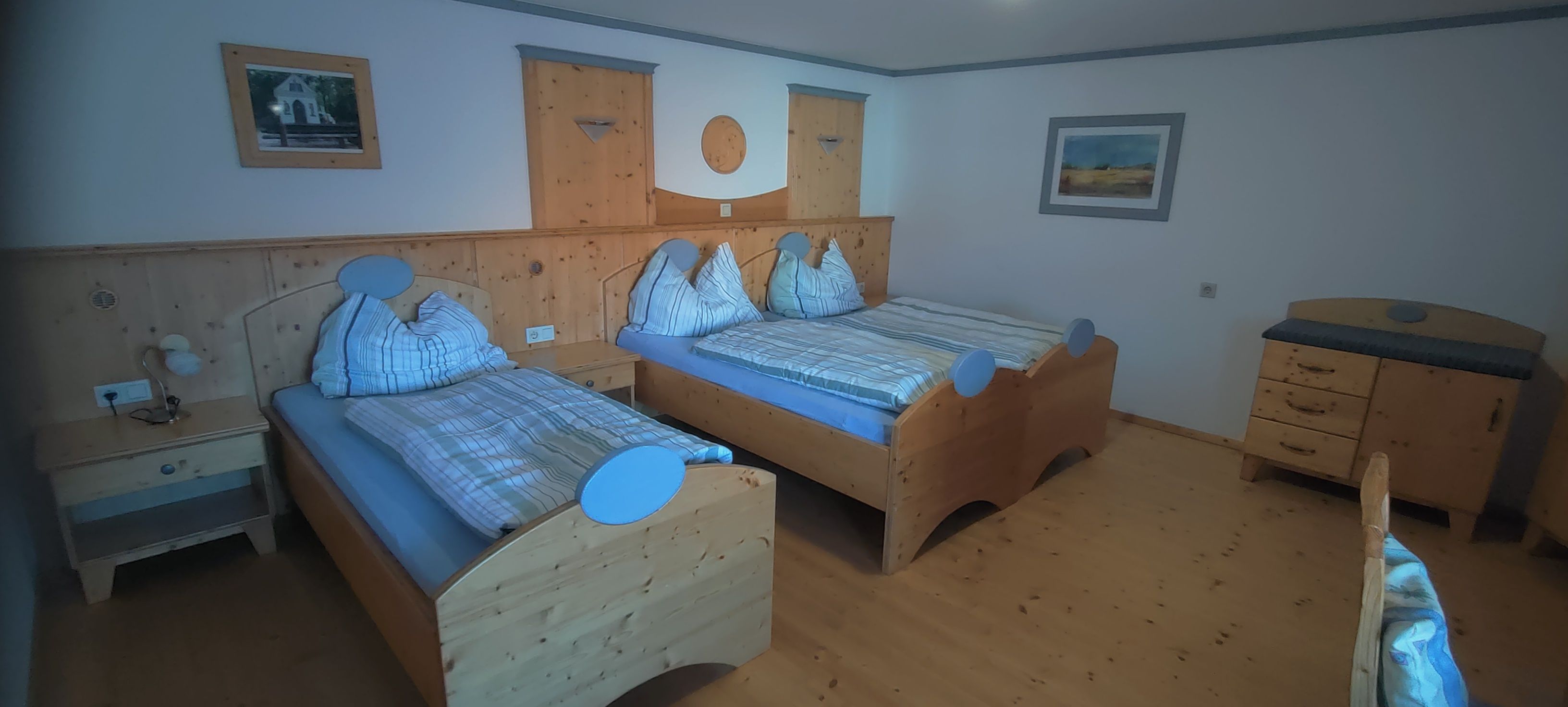 Gemütliches Schlafzimmer mit zwei Einzelbetten aus Holz, Nachttisch und Kommode.