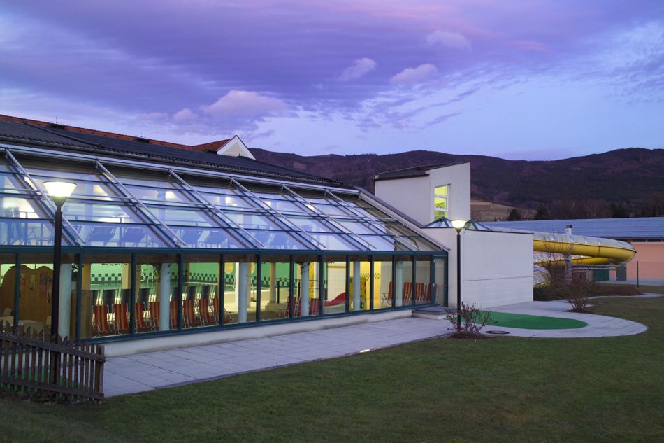Außenansicht des Hallenbads Yspertal bei Dämmerung mit Glasfassade und Rutsche.