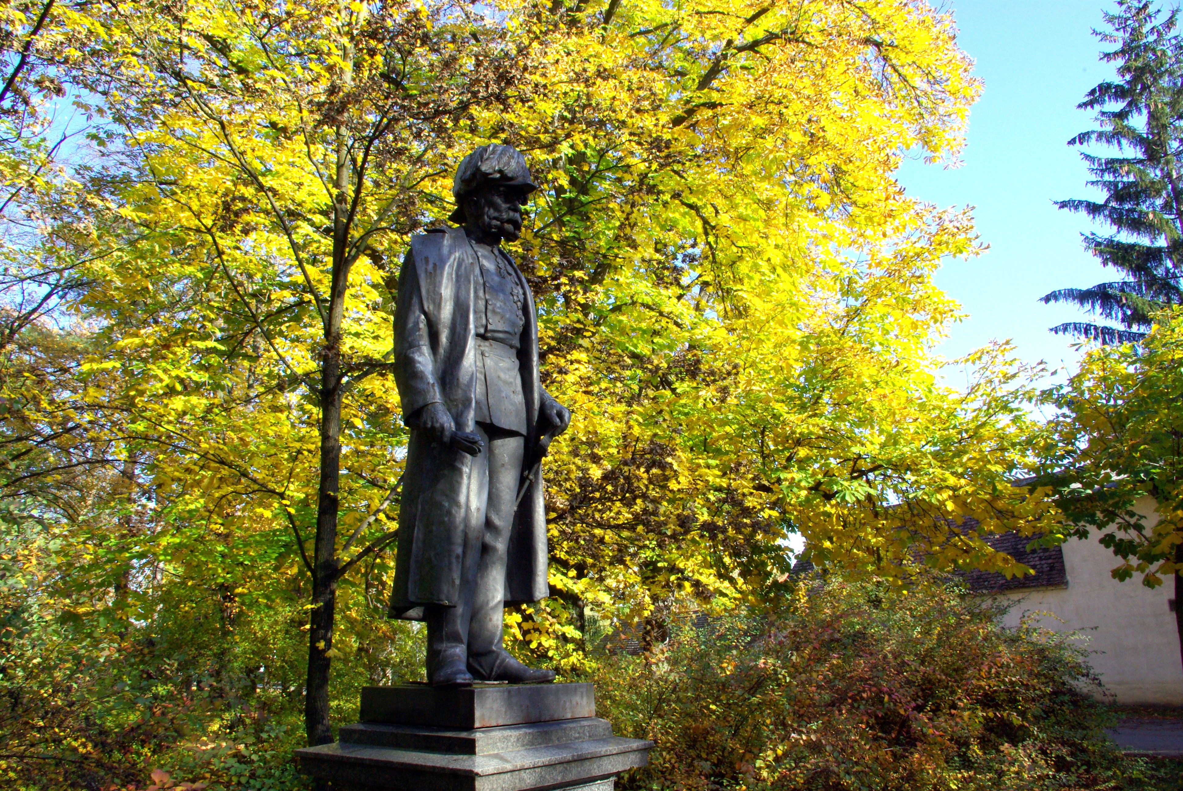 Statue eines Mannes in einem Herbstpark mit gelben Blättern im Hintergrund.