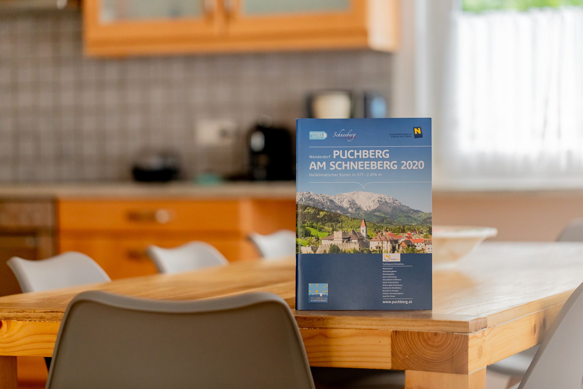 Ein Prospekt von Puchberg am Schneeberg steht auf einem Holztisch in einer Küche.