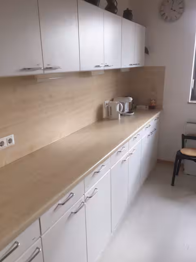 Weiß-Hellbraune Küchenzeile mit viel Stauraum, Wasserkocher und Kaffeemaschine.