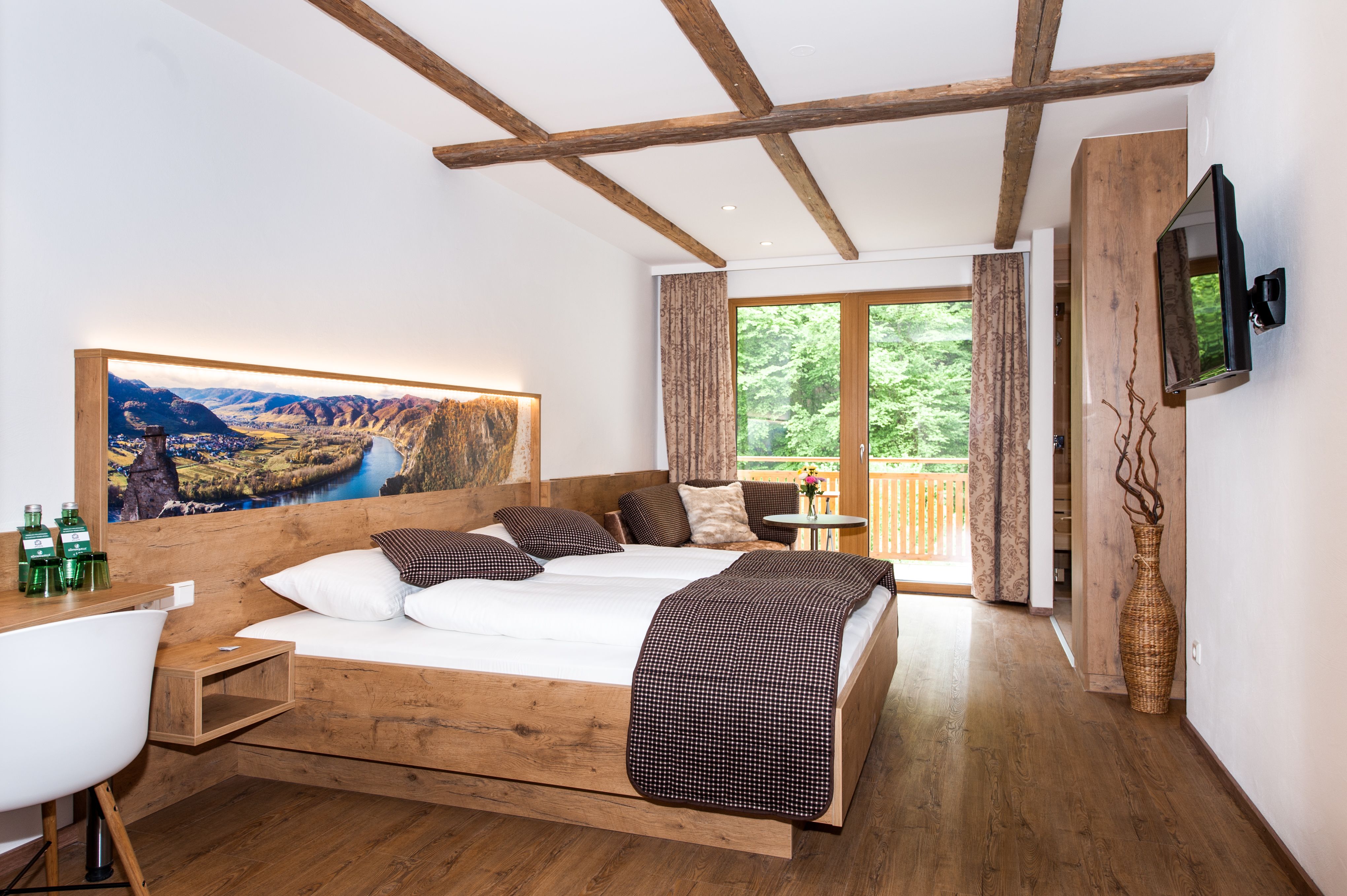 Modernes Hotelzimmer mit Holzmöbeln, großem Bett und Balkon mit Blick ins Grüne.