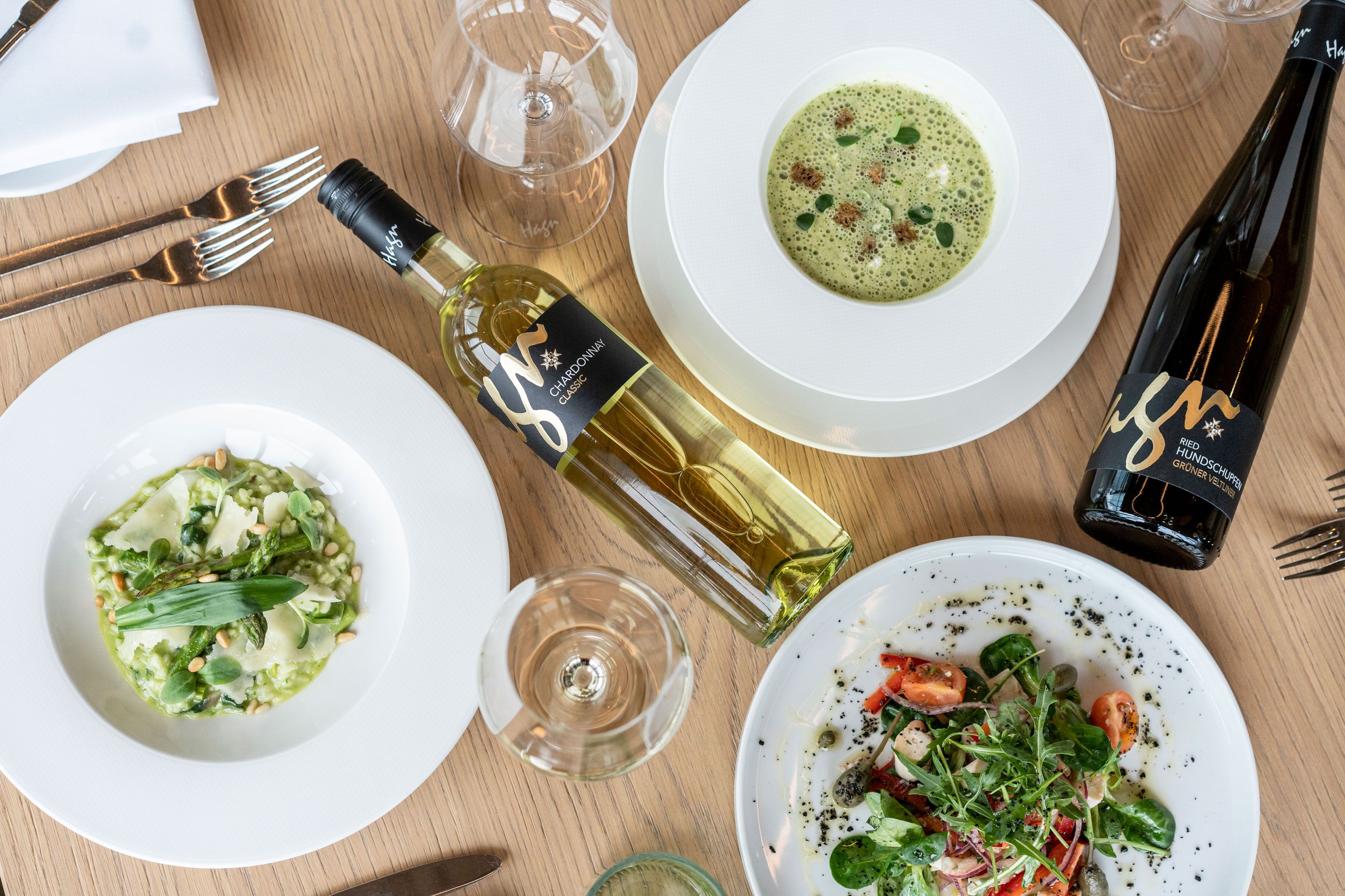 Ein gedeckter Tisch mit zwei Flaschen Wein, einer Suppe, einem Risotto und einem Salat.