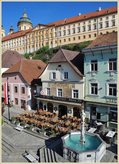 Café mit Terrasse und Brunnen vor einem historischen Gebäude.