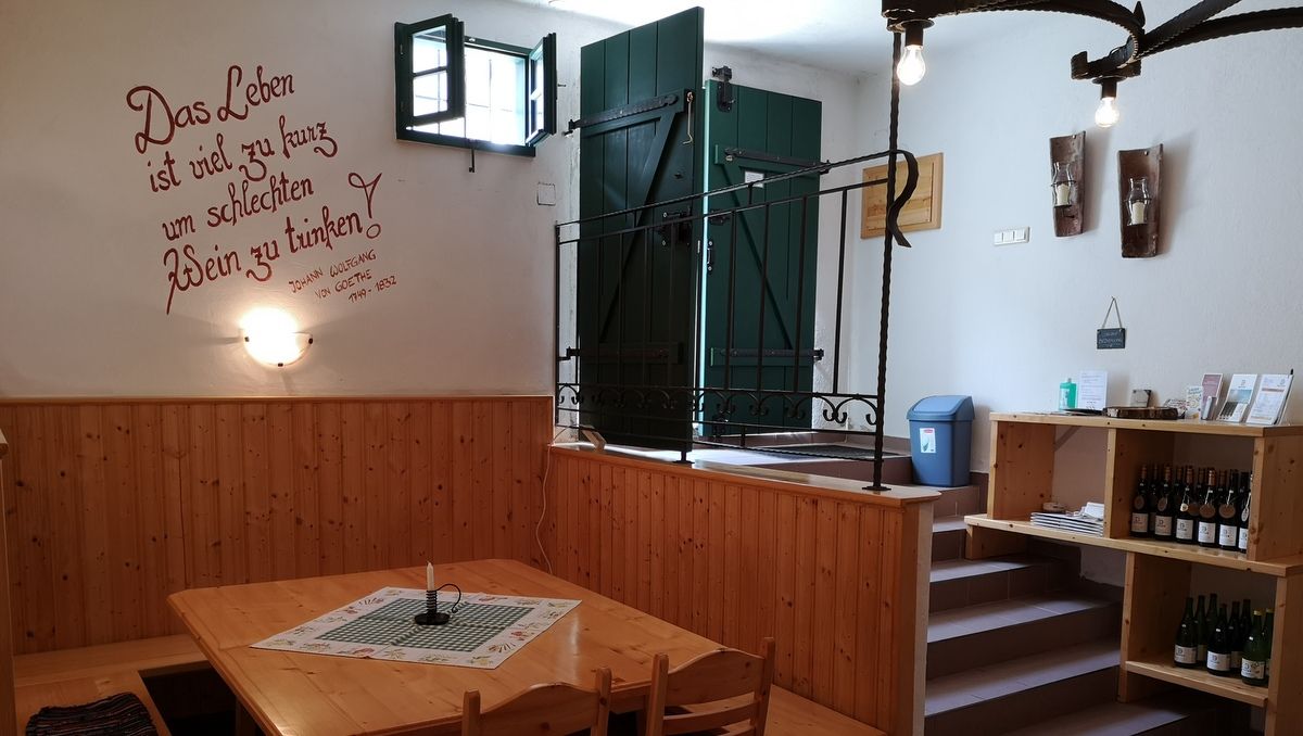 Innenansicht eines gemütlichen Weinkellers mit Holztischen und Regalen, dekoriert mit einem Goethe-Zitat an der Wand.