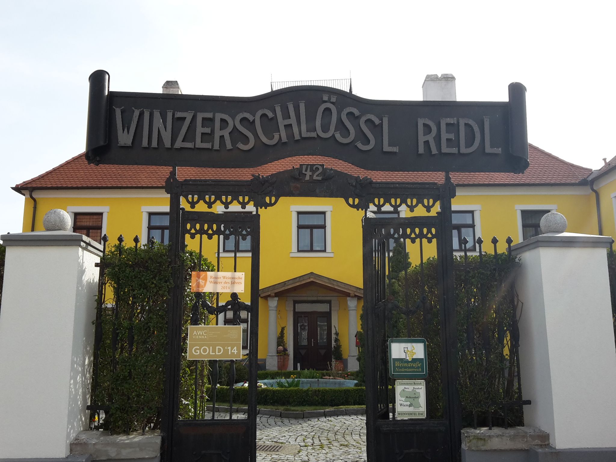 Eingangstor zum Winzerschlössl Redl mit gelbem Gebäude im Hintergrund.