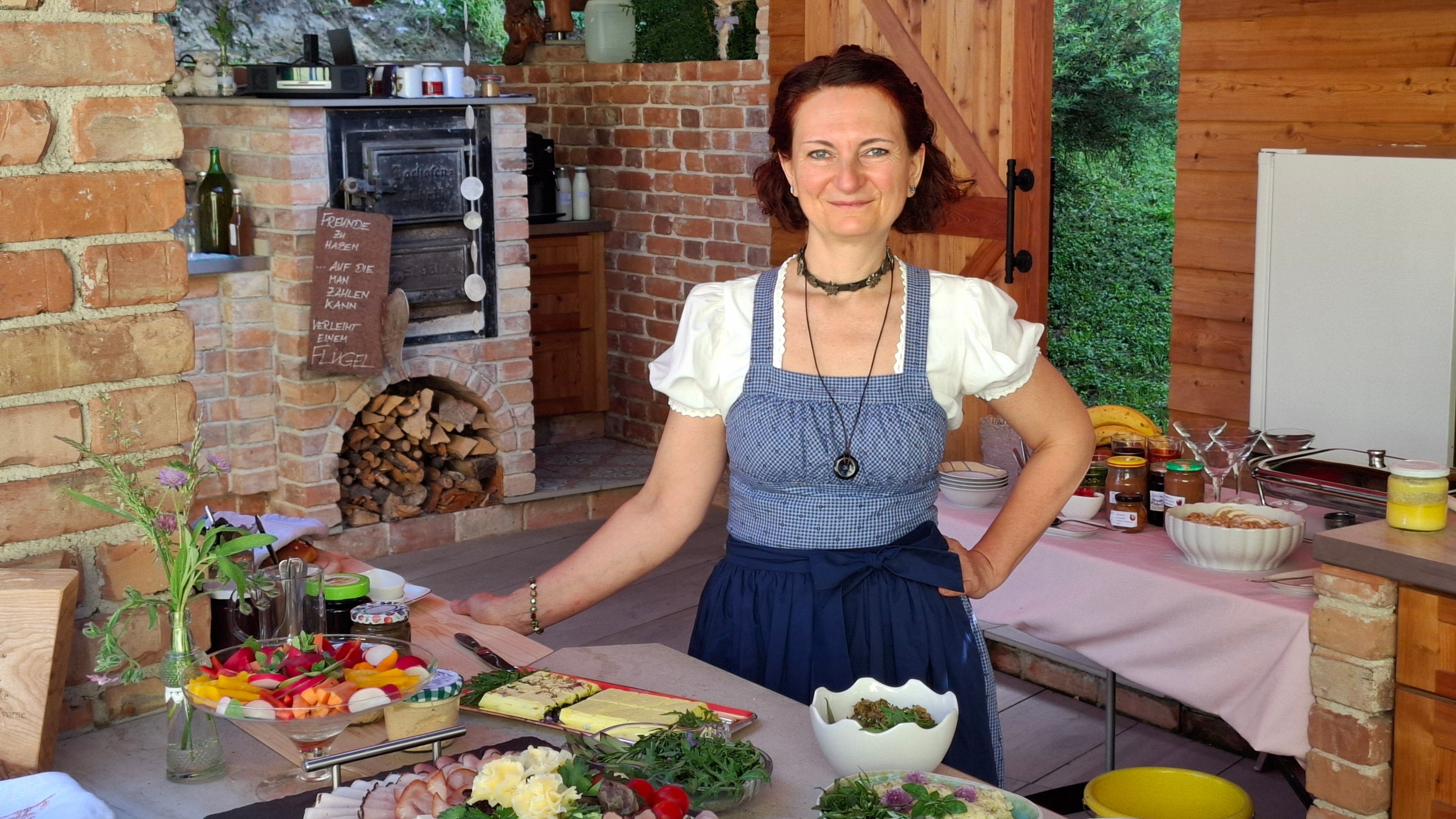 Die Chefin in traditioneller Kleidung in einer rustikalen Küche mit Speisen.