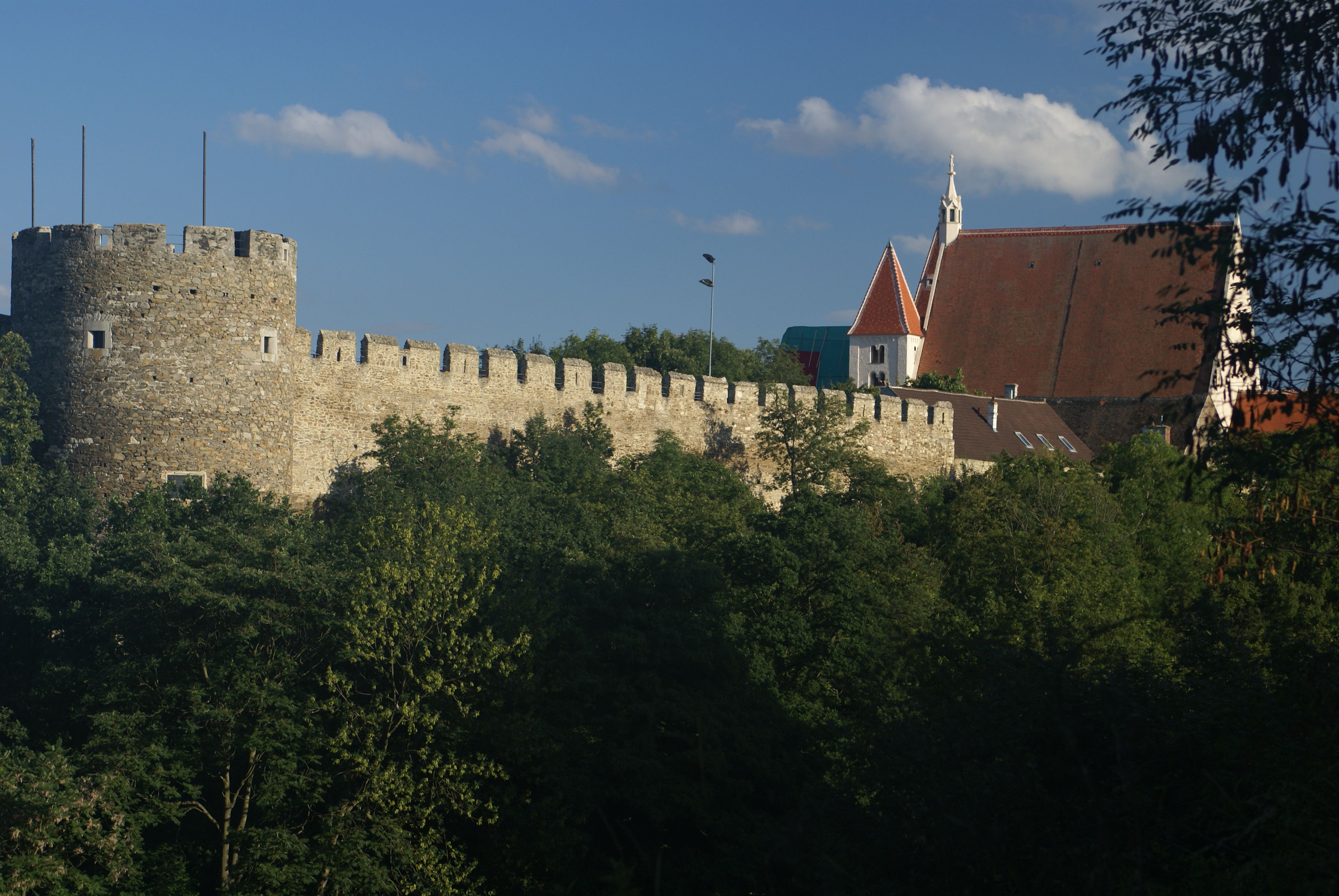 Stadtmauer mit Kanzlerturm und Pfarrkirche im Hintergrund, umgeben von Bäumen.