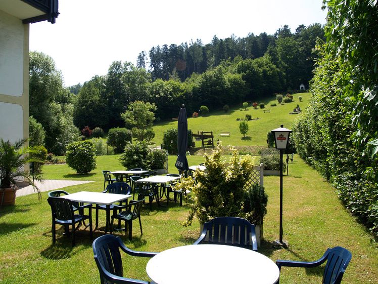 Garten mit Tischen und Stühlen, umgeben von Bäumen und Wiesen.