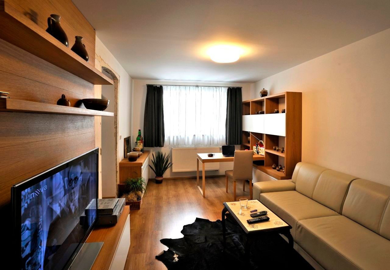 Modern eingerichtetes Wohnzimmer mit Sofa, Fernseher, Schreibtisch und Regalen.