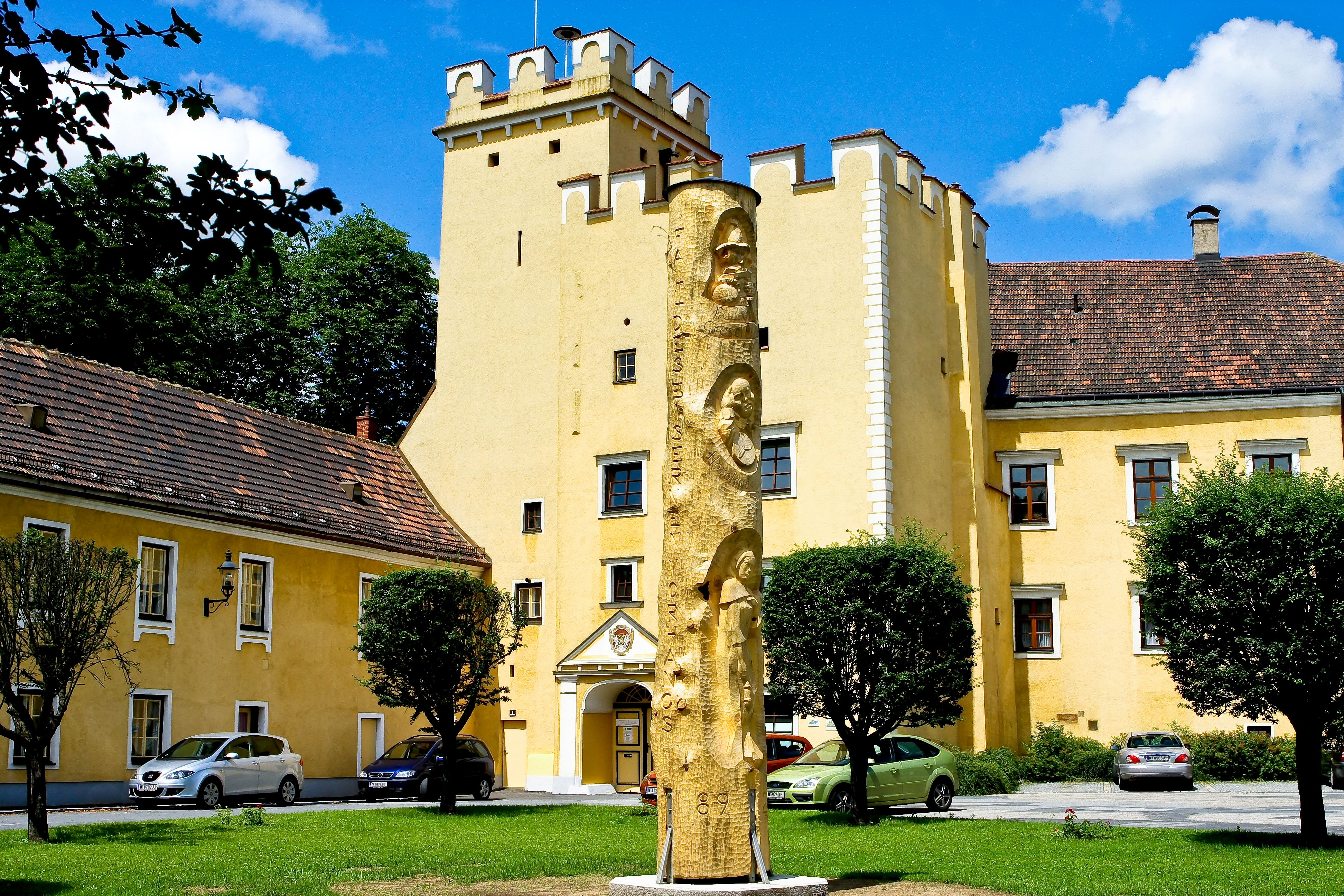 Gelbes Gebäude mit Turm und goldener Skulptur im Vordergrund.
